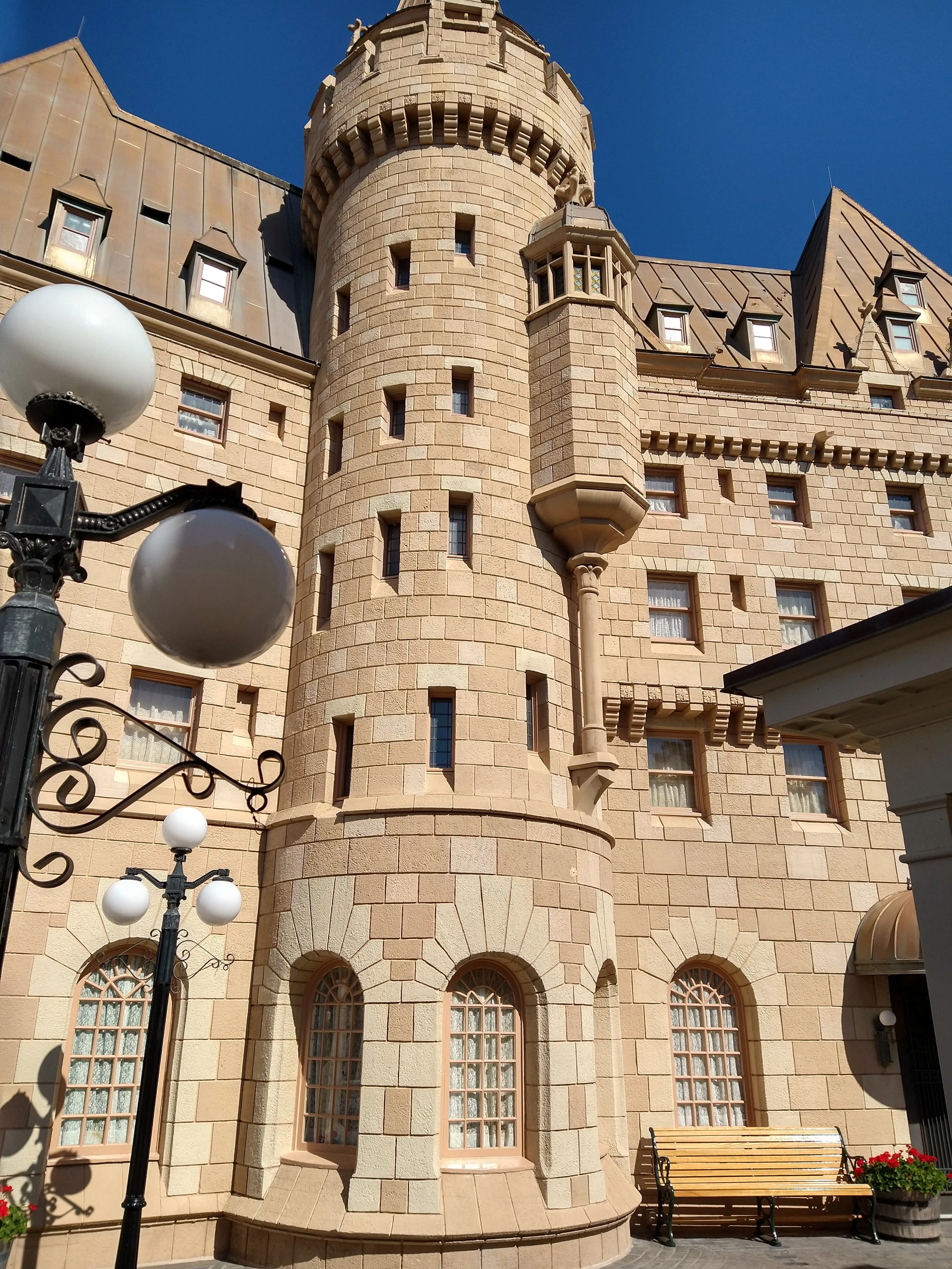 Stone castle-style building with a round tower, arched windows, and decorative details, under a clear blue sky.