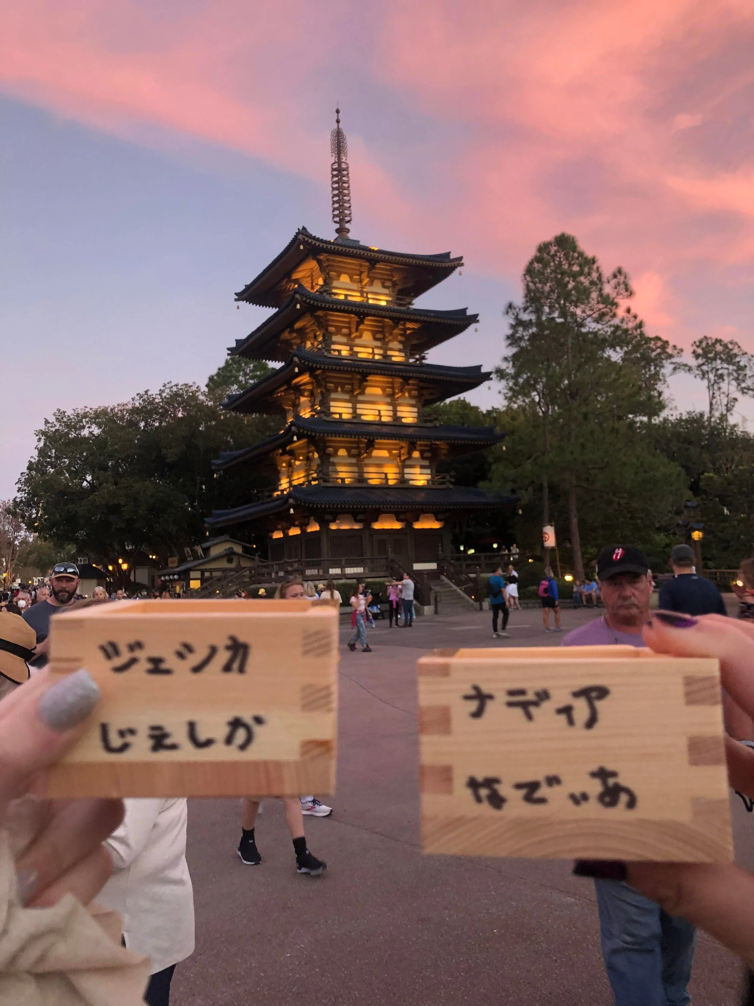 People holding wooden plaques with Japanese writing in front of a multi-tier pagoda during sunset at a traditional Japanese temple.