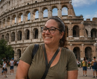 Woman smiling near the Colosseum in Rome, Italy, with other tourists in the background.