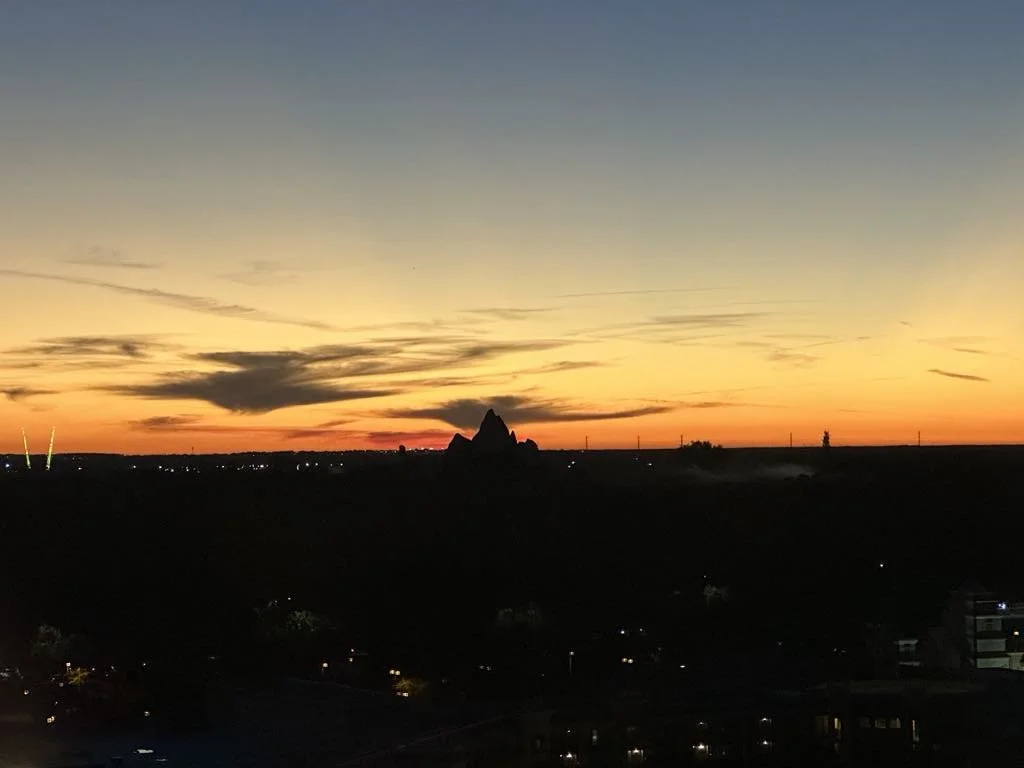 Sunset over a landscape with dark hills, a silhouette of a mountain or rock formation, and a mostly clear sky with some clouds