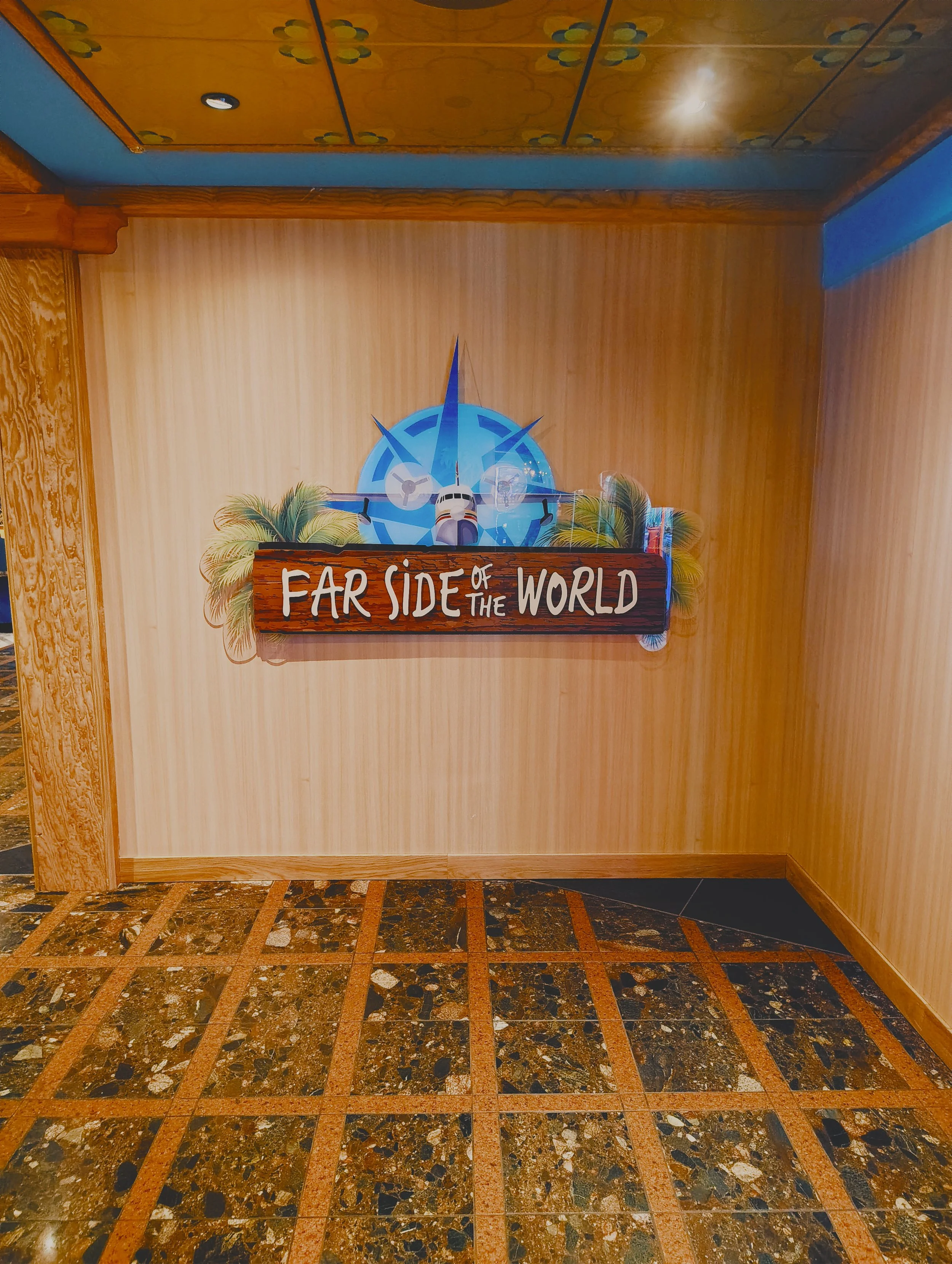 Wall decoration featuring a tropical theme with a sign reading "Far Side of the World" under a colorful compass and airplane, surrounded by palm leaves.