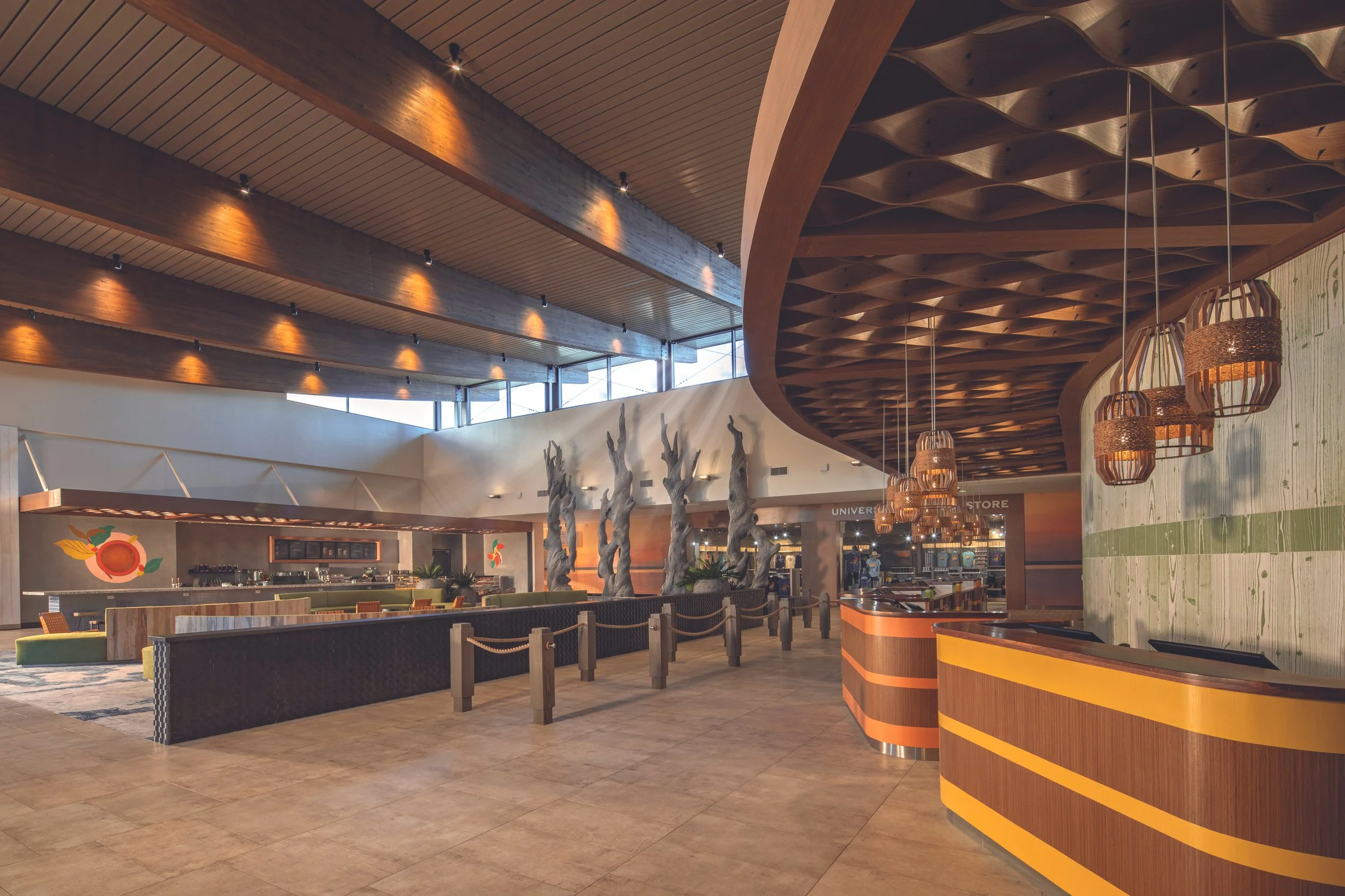 Interior of a modern hotel lobby with wooden ceiling, decorative wood branching sculptures, hanging wicker pendant lights, and a check-in counter.