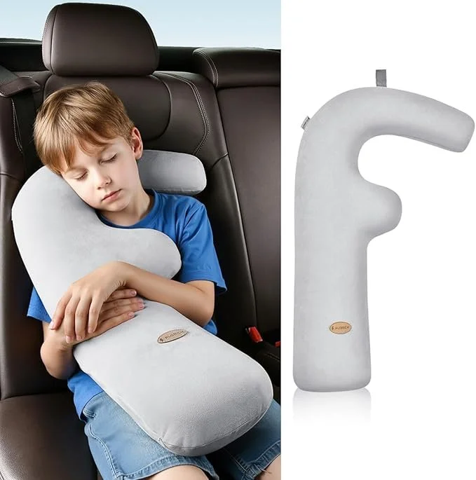 A young boy sleeping comfortably in a car seat with a white travel pillow shaped like an 'L' supporting his head and neck, shown next to the car seat.