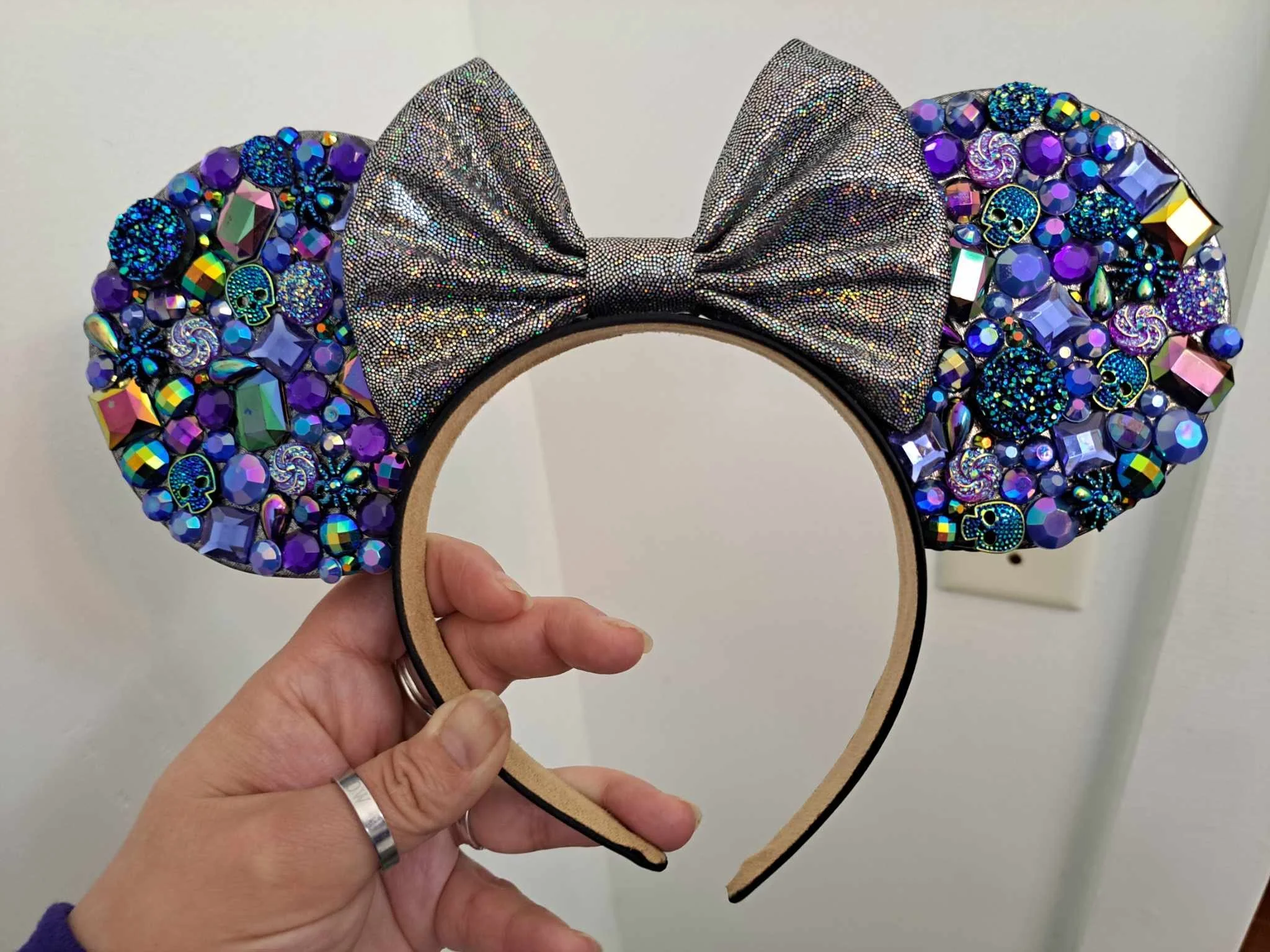 A headband with large purple ear-shaped sections decorated with colorful rhinestones, skulls, and spirals, and a silver glittery bow in the center.