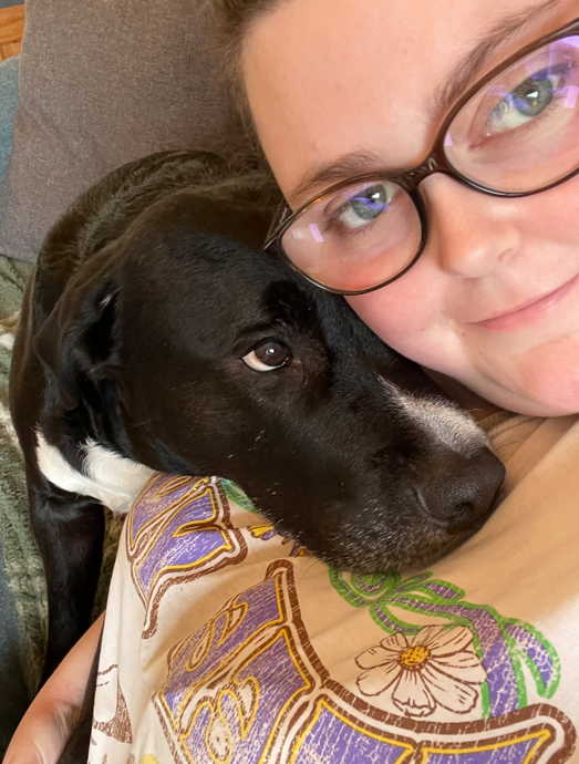 A person with glasses and a puppy resting its head on their chest.