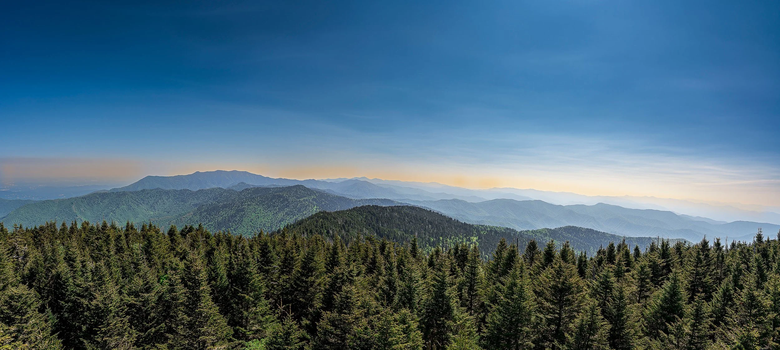Scenic view of green forested mountains under a blue sky at sunrise or sunset.