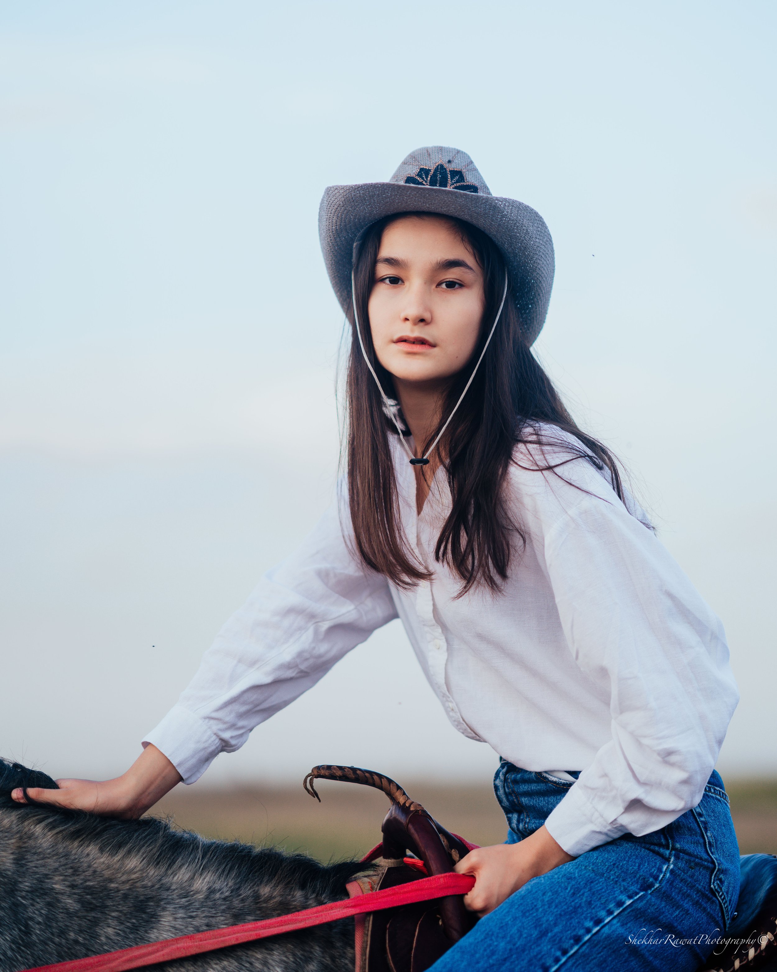 Woman in a cowboy hat riding a horse against a clear sky, lifestyle portrait by Melbourne photographer Shekhar Rawat