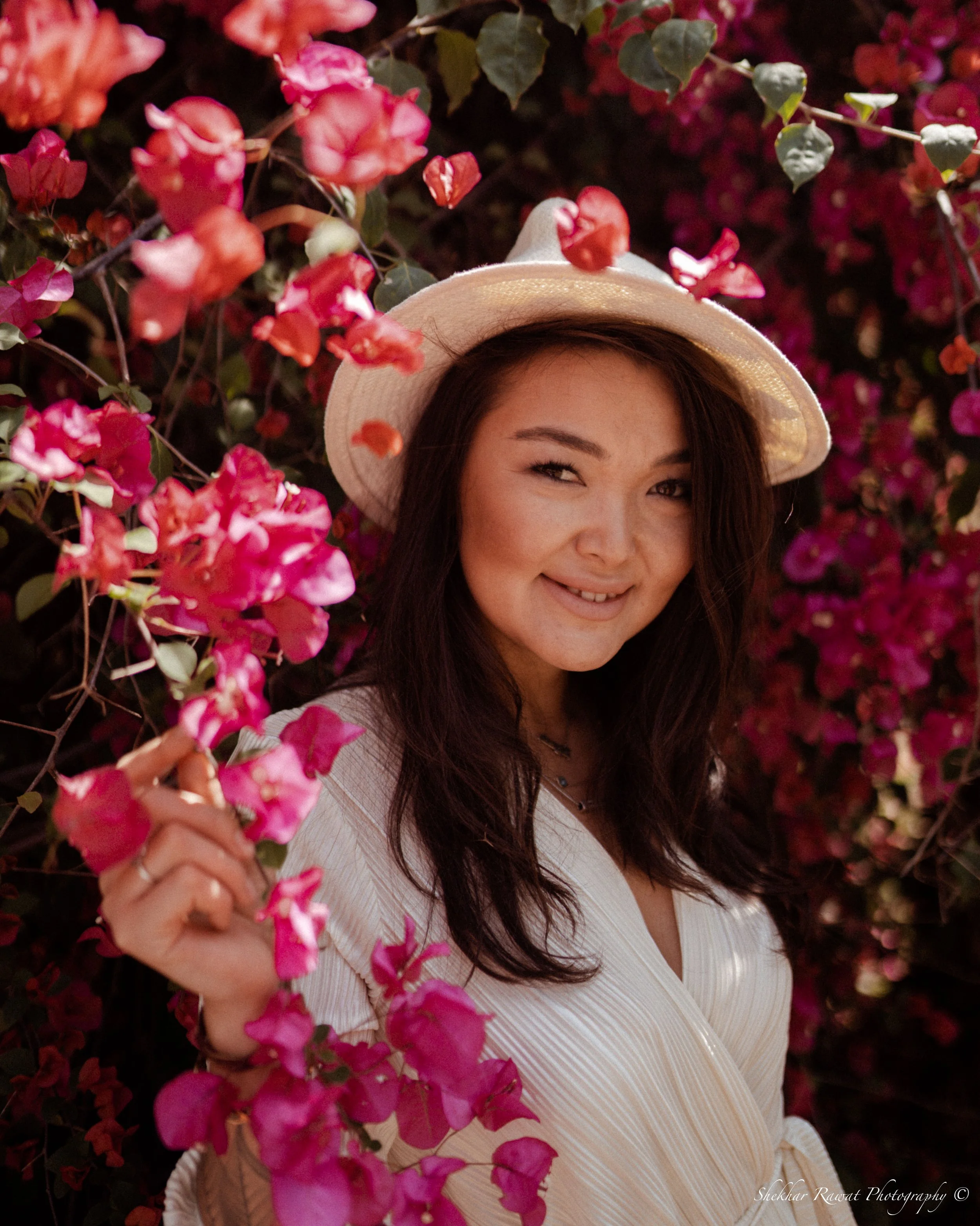 Smiling woman in a sun hat among pink flowers, spring portrait by Melbourne photographer Shekhar Rawat