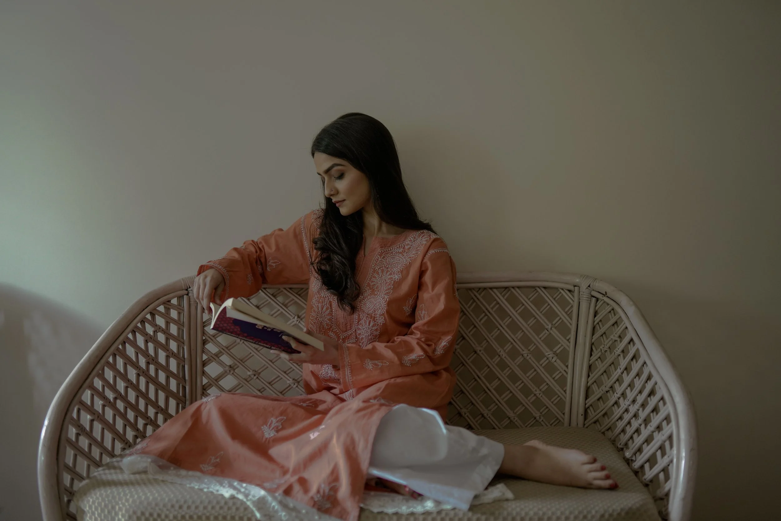 Model in a traditional orange outfit reading on a wicker chair, Indian fashion shoot by Melbourne photographer Shekhar Rawat