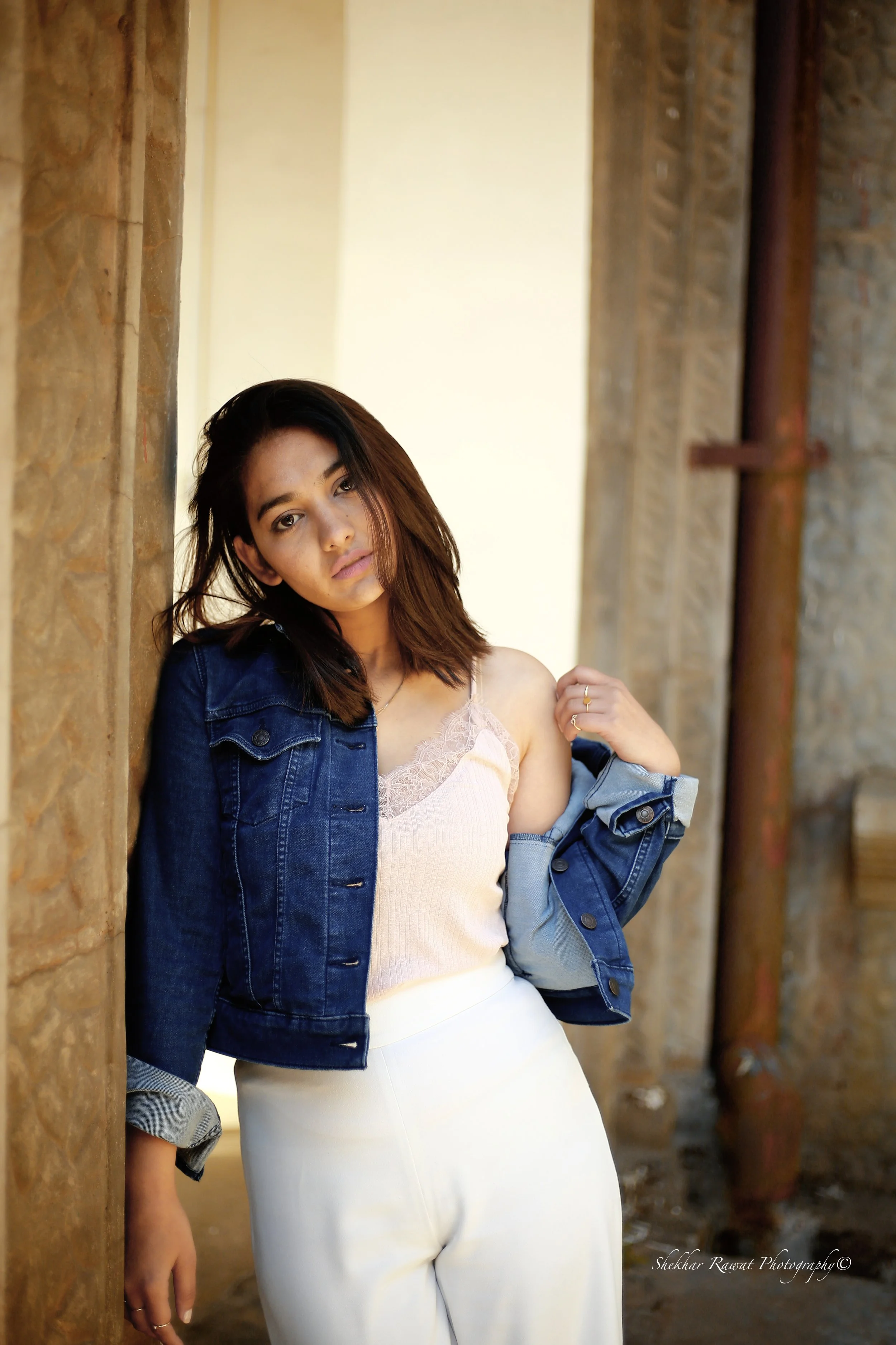 Model in a white dress and denim jacket against a brick wall, urban portrait by Melbourne photographer Shekhar Rawat