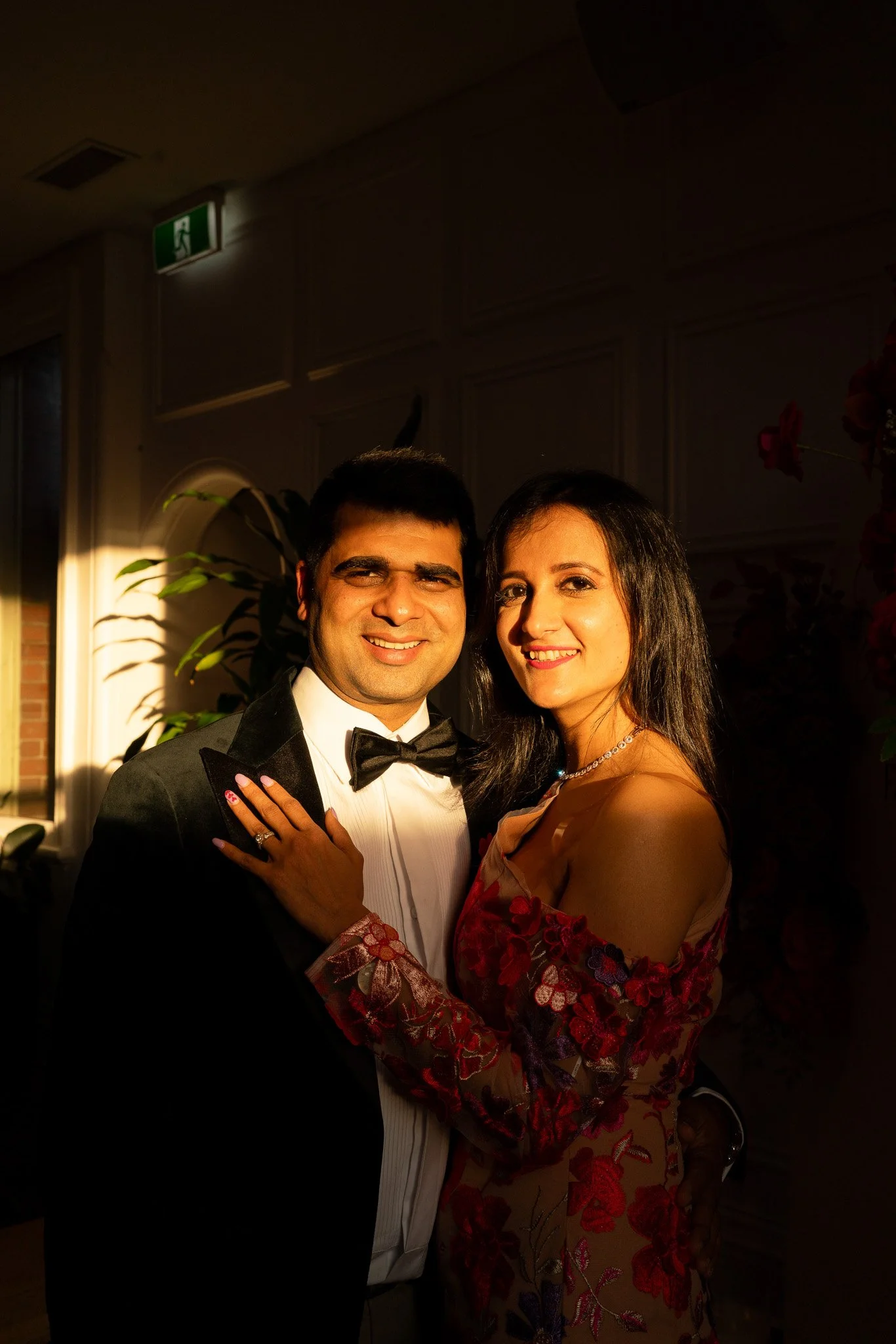 A man and woman dressed in formal attire, smiling, standing close together indoors.