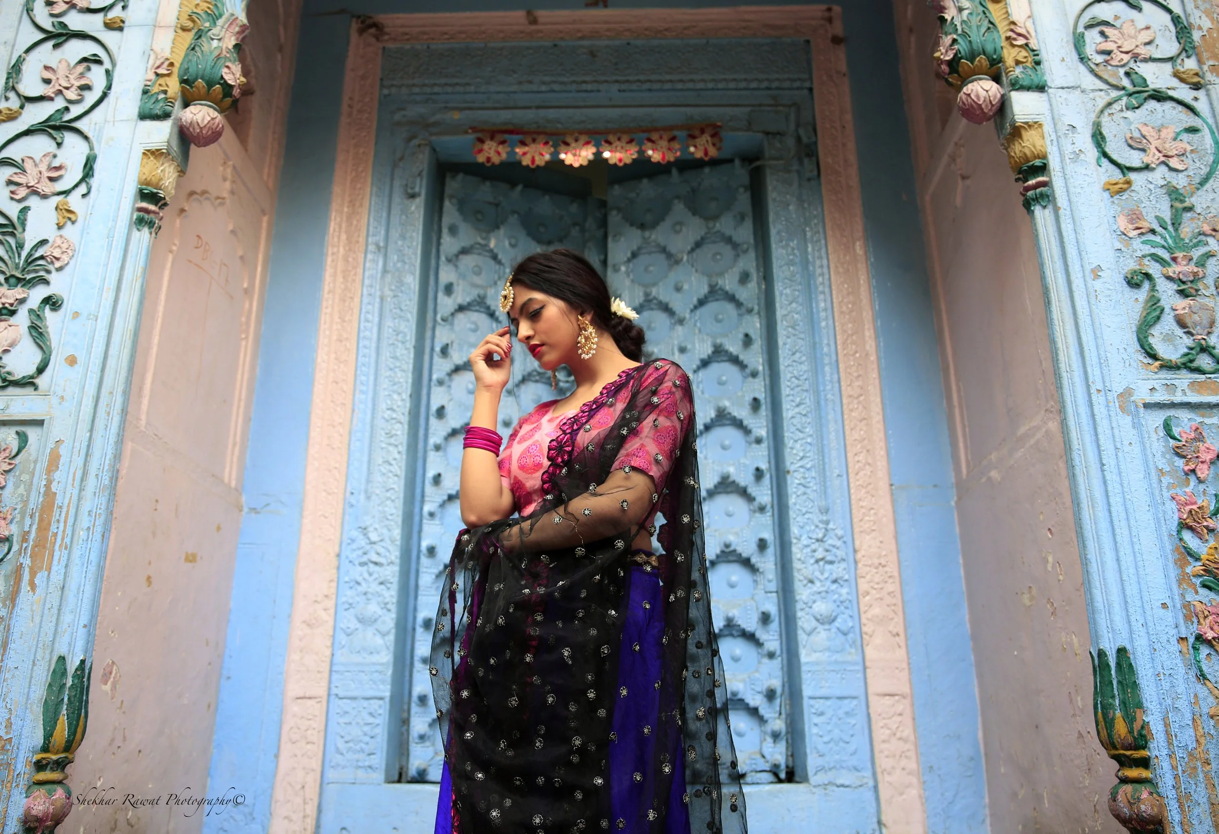 Woman in a traditional magenta and black outfit at a painted blue doorway, Indian portrait by Melbourne photographer Shekhar Rawat