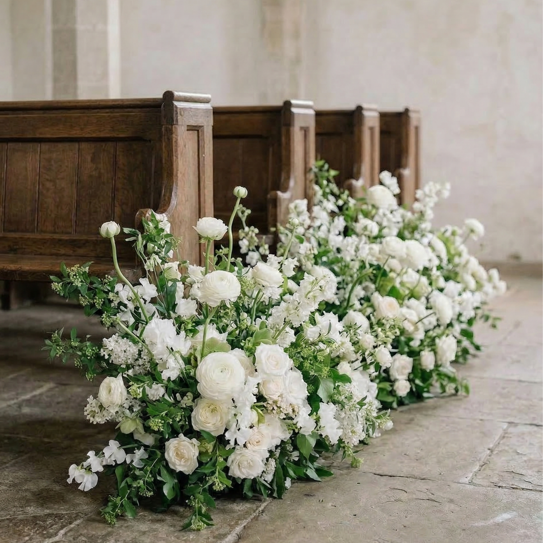 White floral arrangements on the floor in front of wooden pews inside a church.