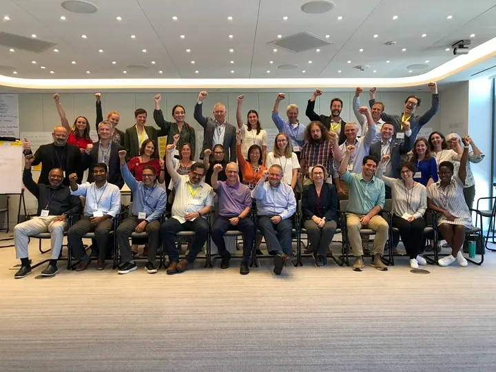 The Workshop participants in a group, three rows deep and about 10–15 people wide, lifting their fists to celebrate two days of hard work.