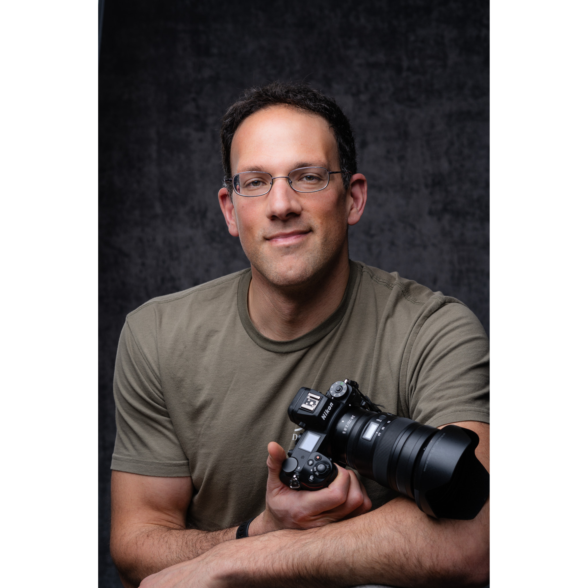 A man holding a camera smiles.