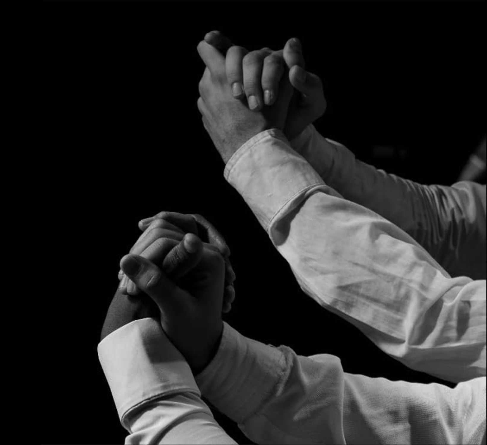 Two pairs of clasped hands, one above the other, isolated on a black background, wearing white sleeves.