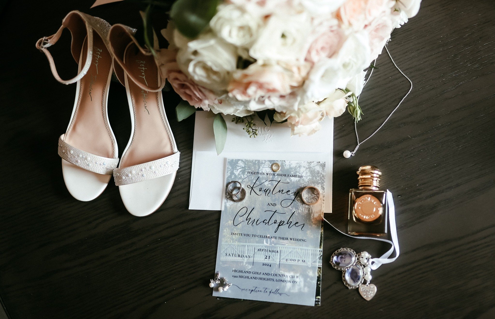Flat lay of wedding shoes, perfume, invitation, and floral bouquet details at London Ontario wedding.