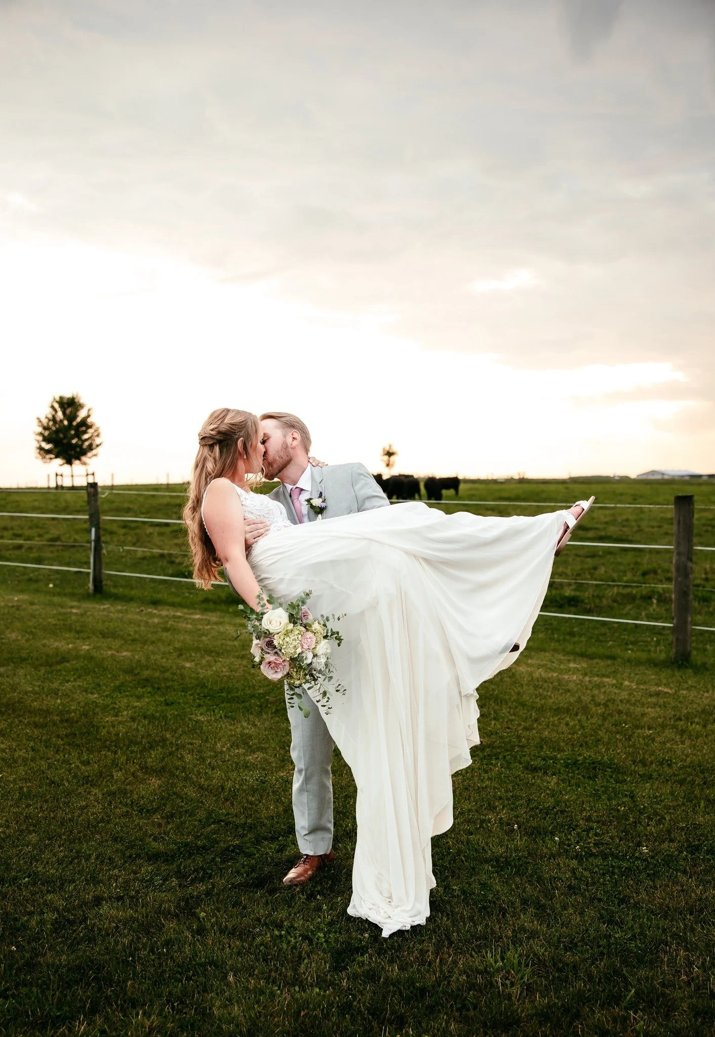 Groom lifting bride in his arms outdoors, joyful wedding moment in London Ontario.