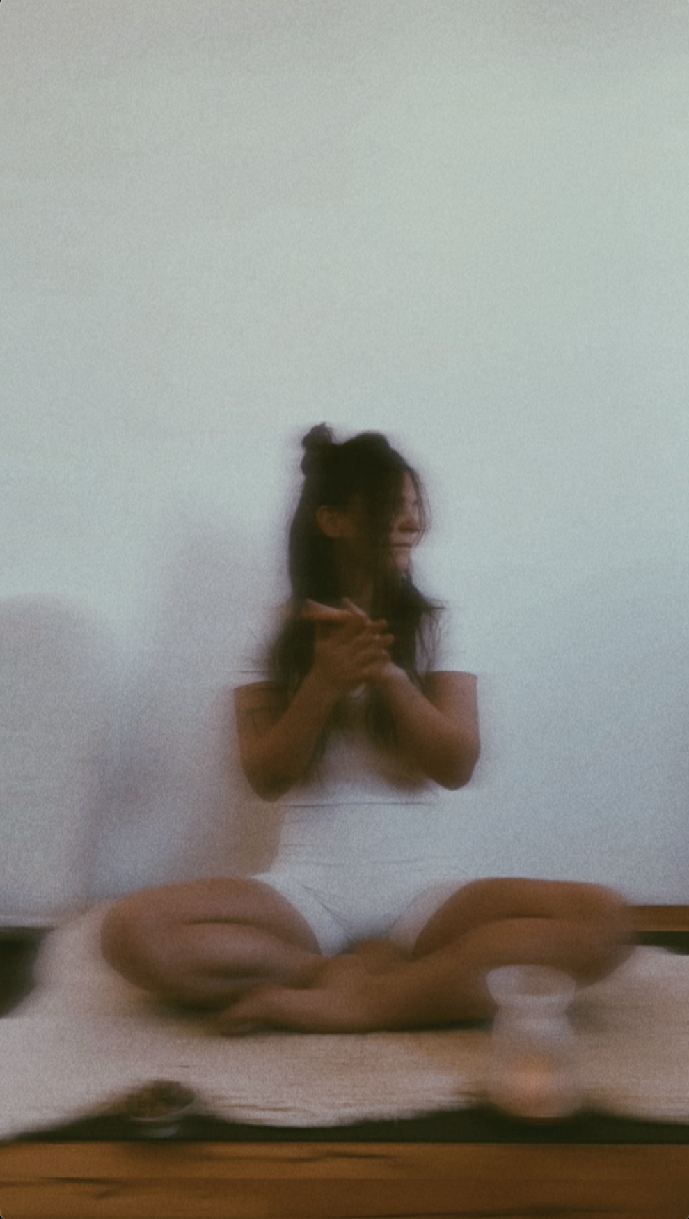 Eine junge Frau sitzt im Schneidersitz auf einem Schafsfell und lächelt, während sie eine Vagus-Ohrmassage praktiziert.