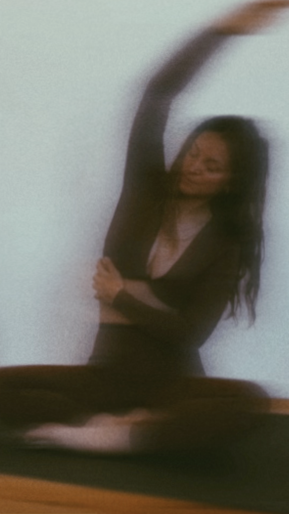 Eine Frau mit welligen, dunklen Haaren praktiziert somatisches Yoga, trägt ein dunkelrotes Outfit, wirkt entspannt und lächelt leicht.