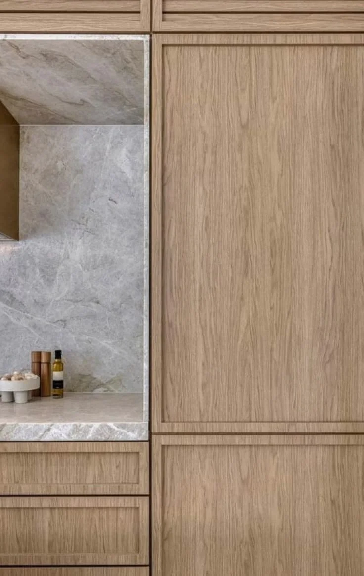 Close-up of a modern kitchen cabinet with wood finish, featuring a marble countertop and a few kitchen items including bottles and a container.