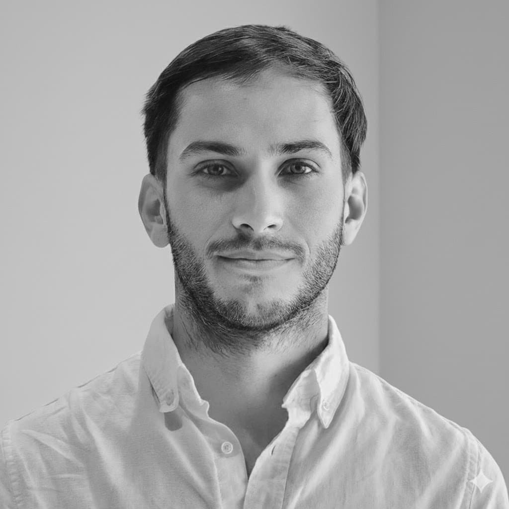 A black-and-white portrait of a young man with short dark hair, light facial hair, and wearing a collared shirt, looking directly at the camera.