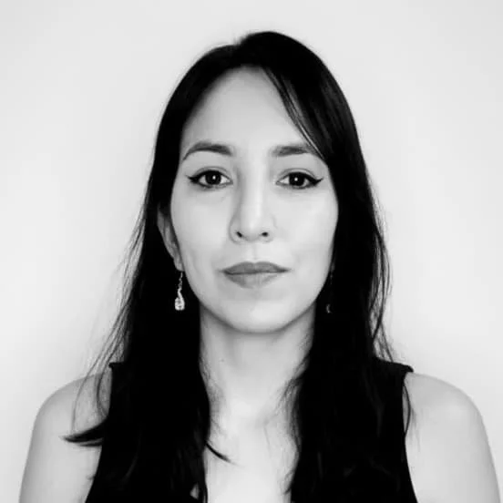 Black and white portrait of a woman with long dark hair, wearing earrings and a sleeveless top, against a plain background.