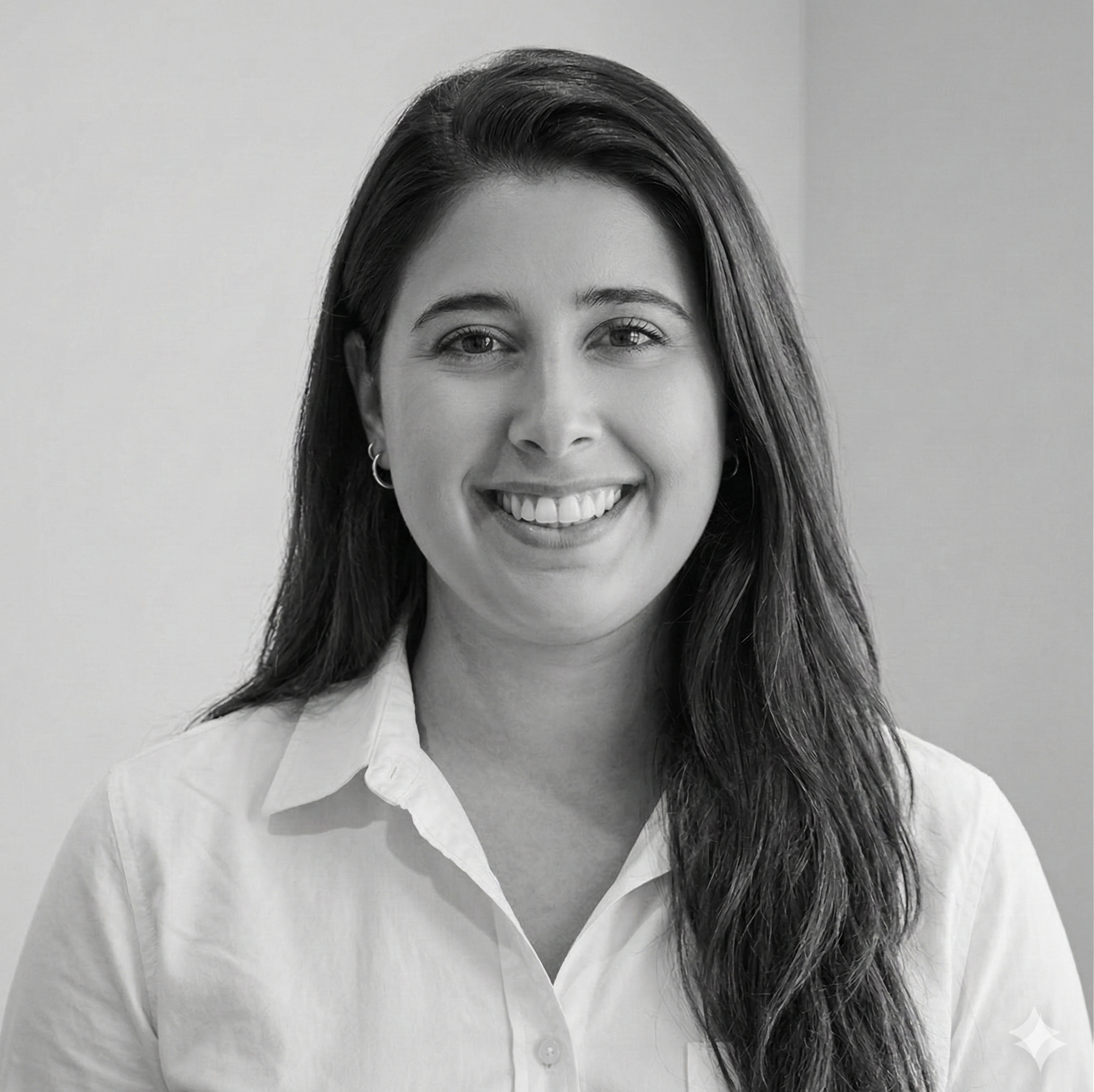 Black and white photo of a woman with long dark hair wearing a white collared shirt, smiling at the camera.