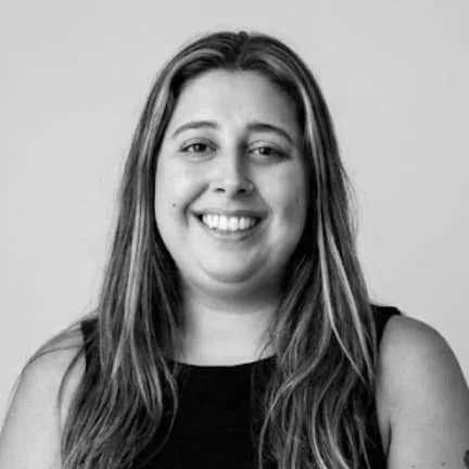 Black and white portrait of a woman with long hair, smiling showing her teeth, wearing a sleeveless top.