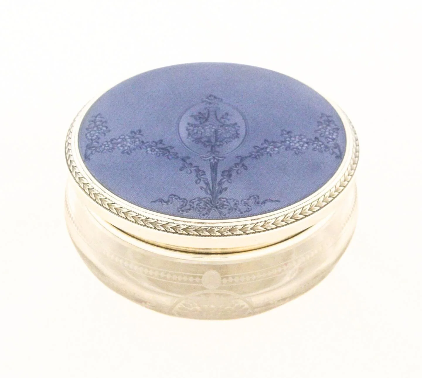 A marriage of two great decorative arts: luminous cut crystal crowned with a finely worked sterling silver and deep cobalt-blue enamel lid. 
This elegant powder jar showcases everything we love about early luxury accessories&mdash;hand-engraved flora