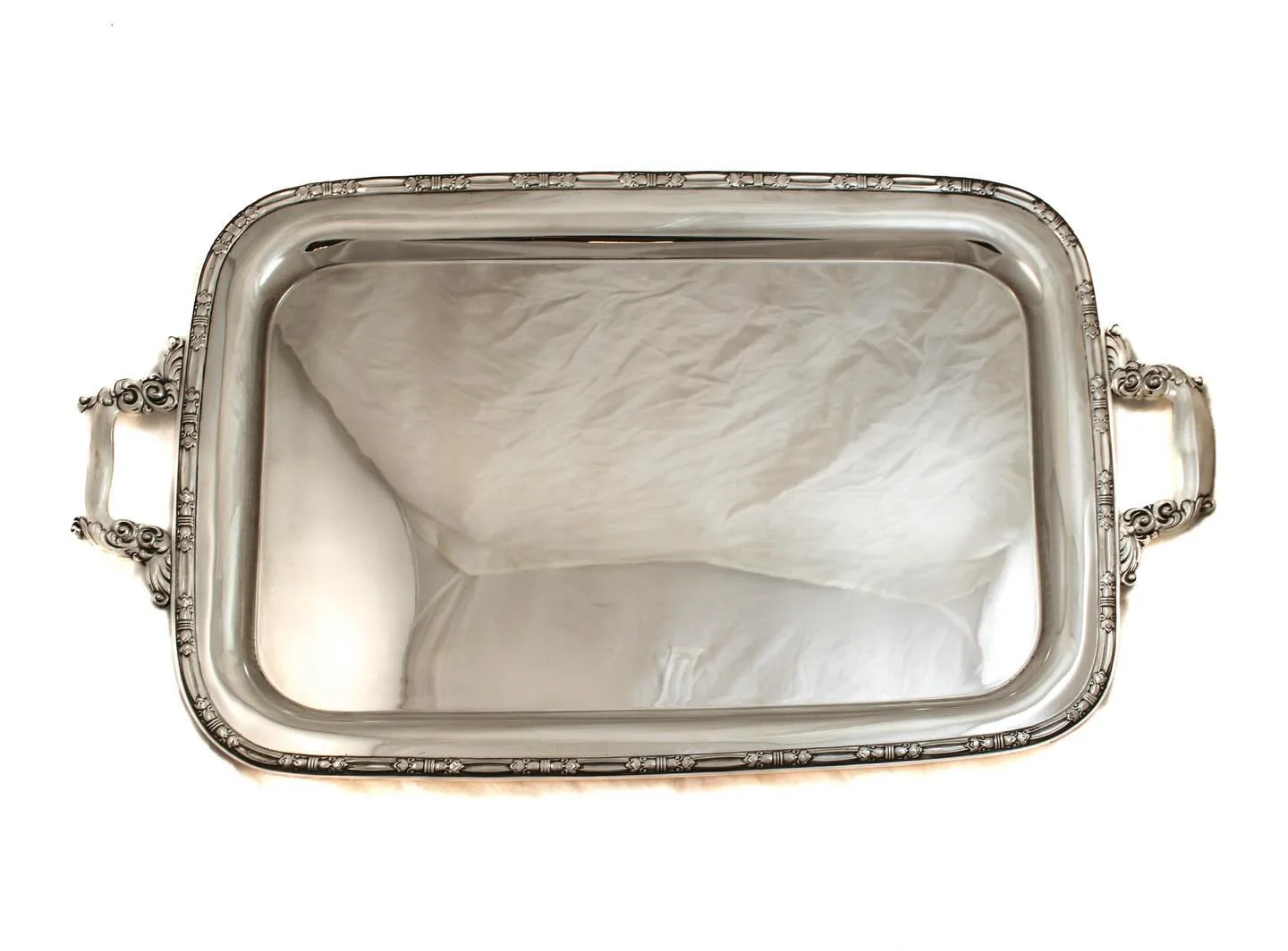Understated elegance never goes out of style.
This beautifully proportioned sterling silver serving tray features a refined border of repeating classical motifs and substantial scrolled handles that lend both presence and balance. The clean, mirror-f