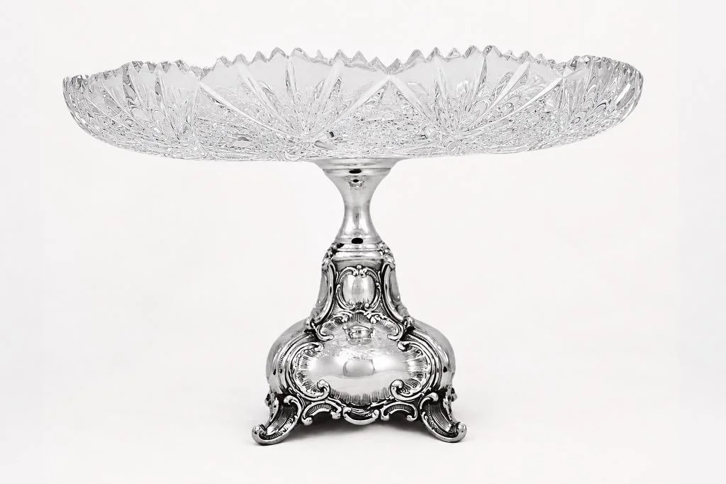 A striking marriage of brilliance and craftsmanship, this magnificent cut crystal cake stand rests upon an ornate sterling silver base rich with flowing repouss&eacute; detail and elegant scrollwork. The dazzling crystal bowl is deeply hand-cut with 