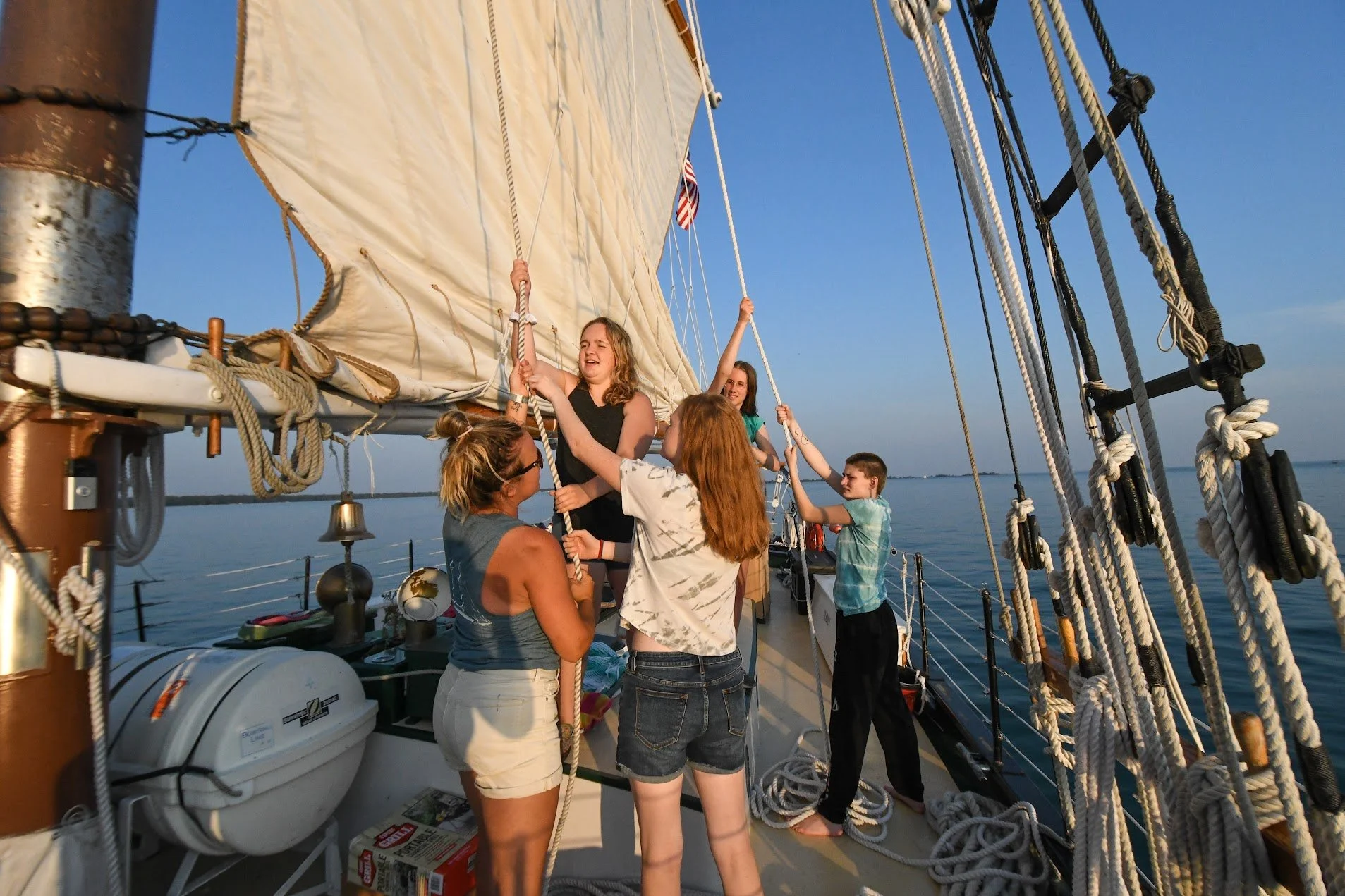 Group of people hoisting sails on a sailboat at sea.