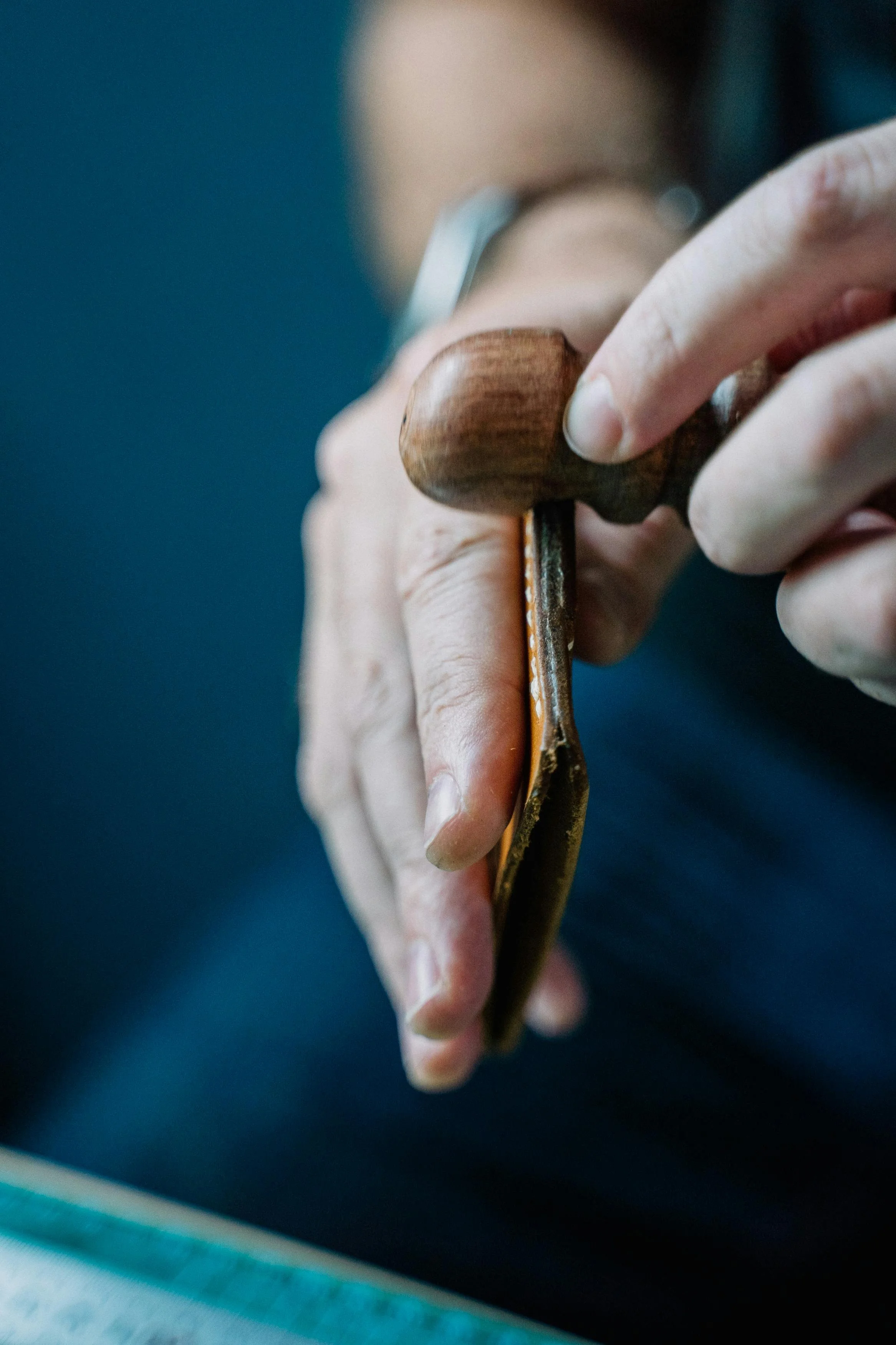 Une personne utilise un outil en bois pour découper ou tailler un matériau, probablement du cuir ou du bois, sur une surface sombre.