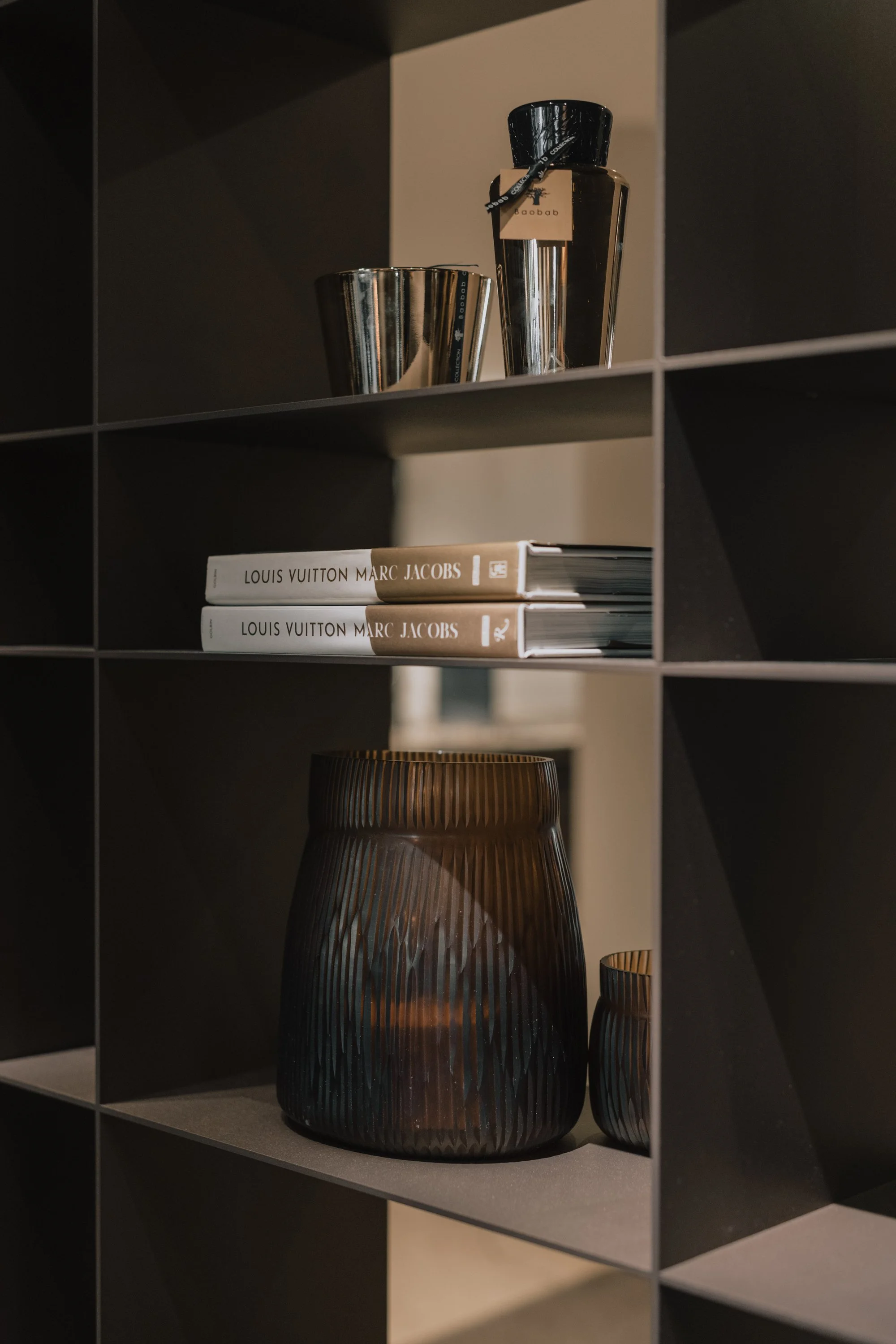 Regal mit schwarzen quadratischen Fächern, darin befinden sich Dekorationsgegenstände, Bücher, eine Glasvase und eine Duftkerze.