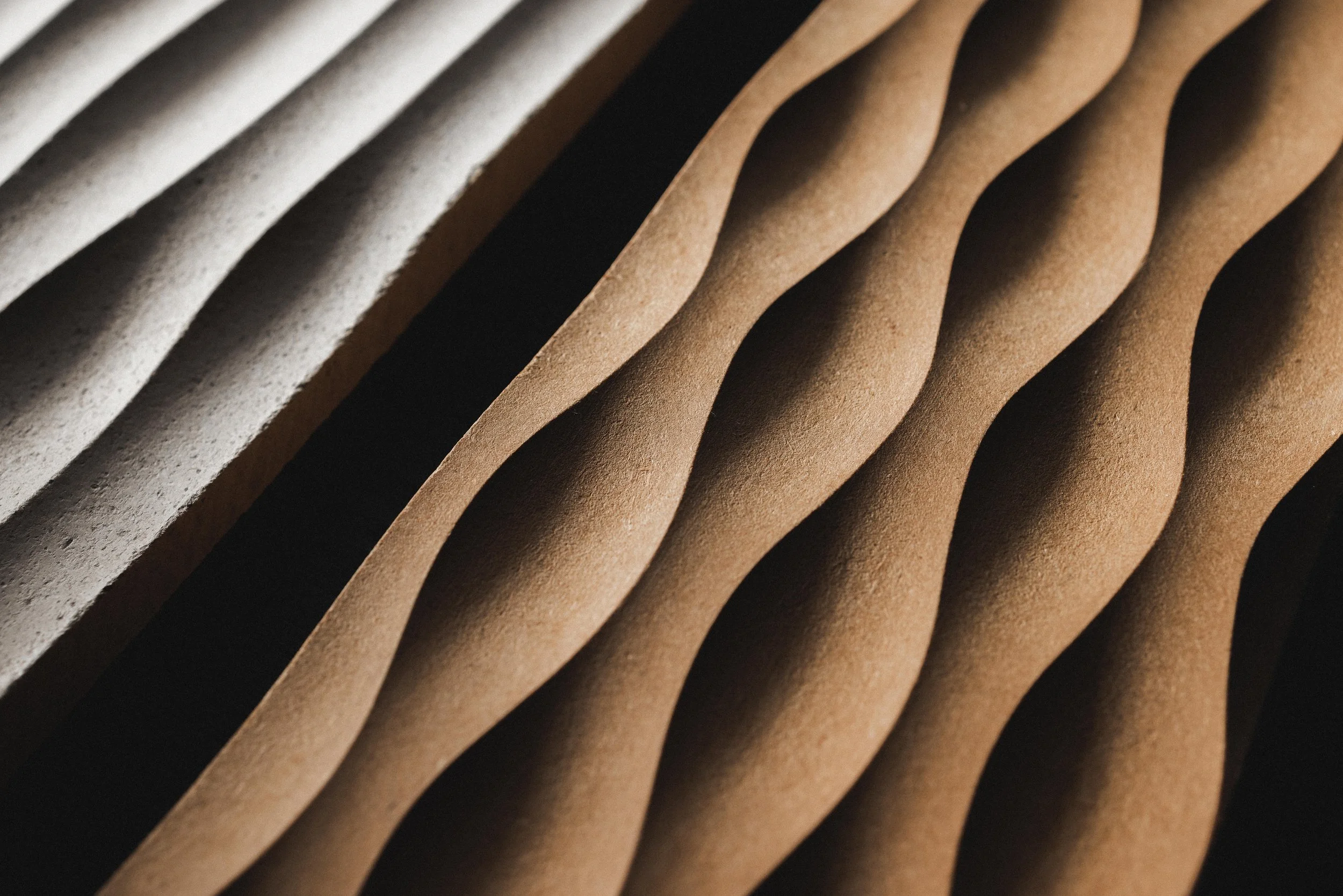 Nahaufnahme von rillenförmigen, gewellten Oberflächen in verschiedenen Erdtönen, vermutlich aus Papier oder Karton.