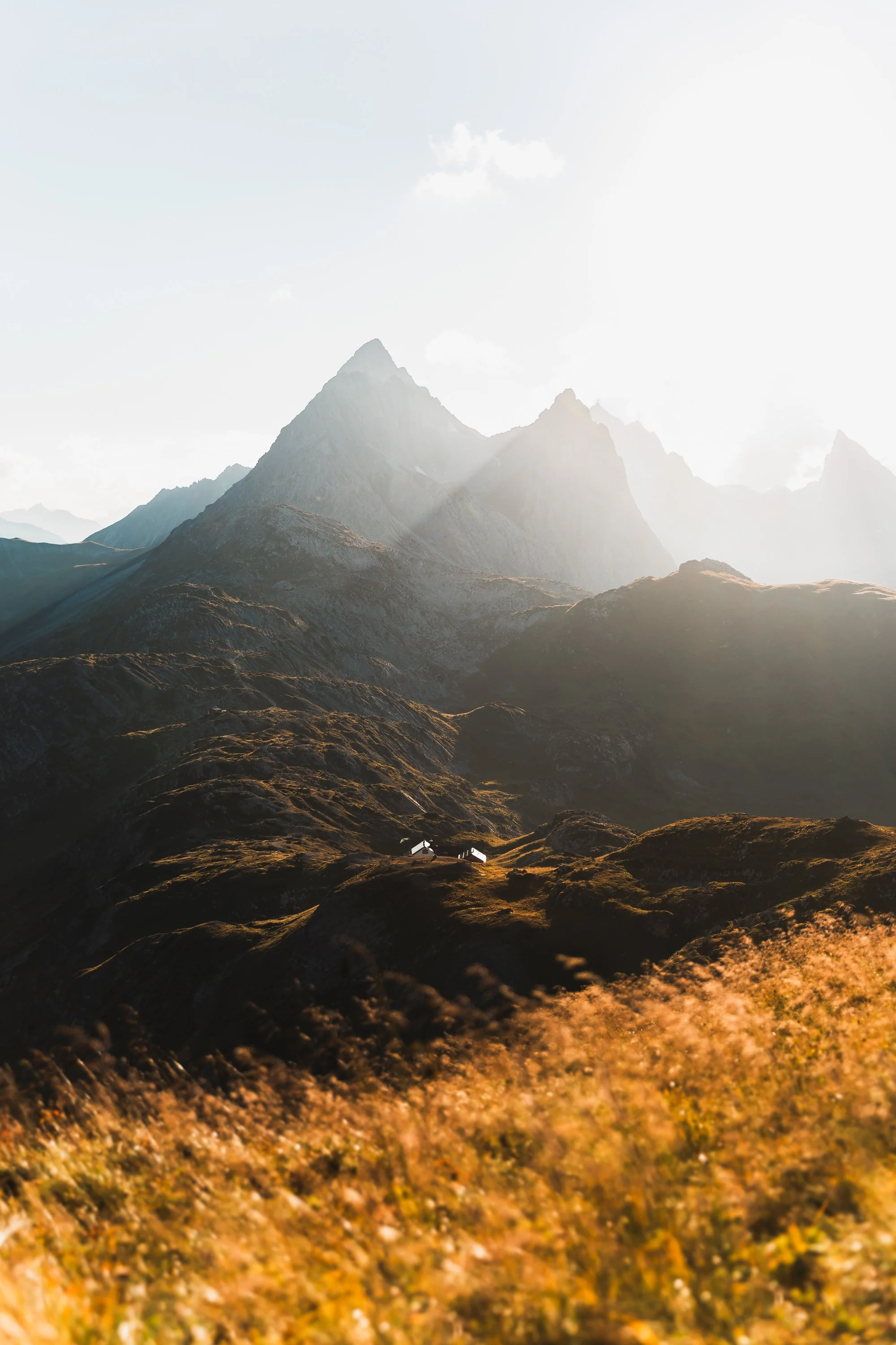 Eine Berglandschaft mit hohen Bergen, die im Sonnenlicht leuchten, und einem kleinen Haus im Tal.