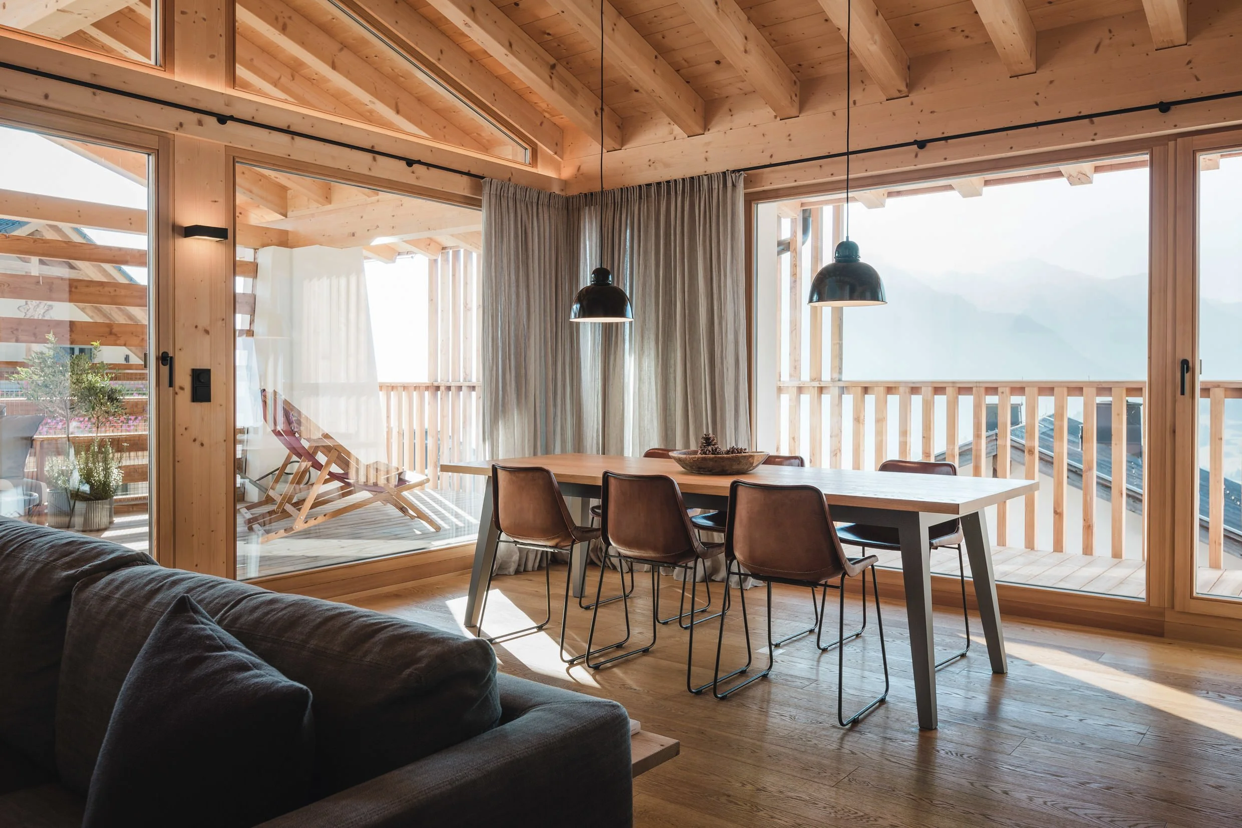 Gemütliches Esszimmer mit Holzmöbeln, großen Fenstern und Blick auf einen Balkon mit Laube und Bergblick.