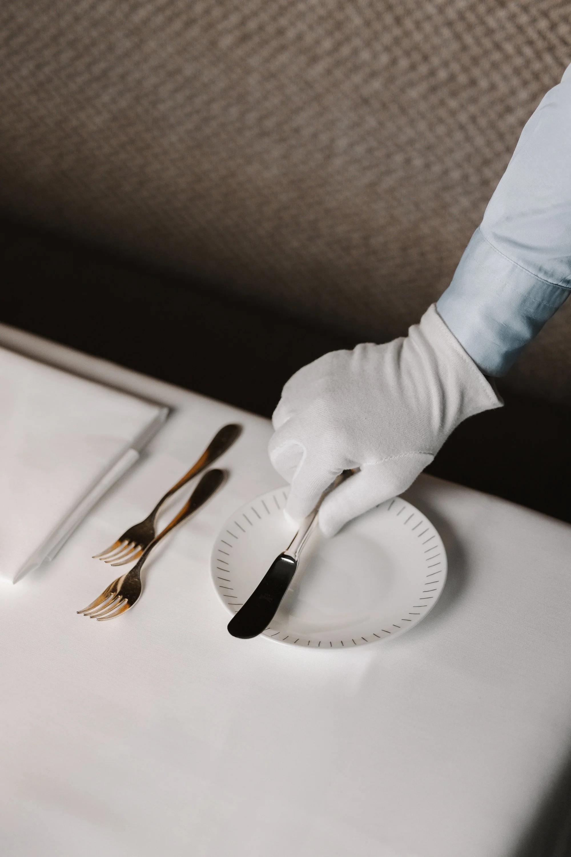 Eine Person in weißem Handschuh deckt einen Teller mit einem Messer bei einem formellen Abendessen ab.