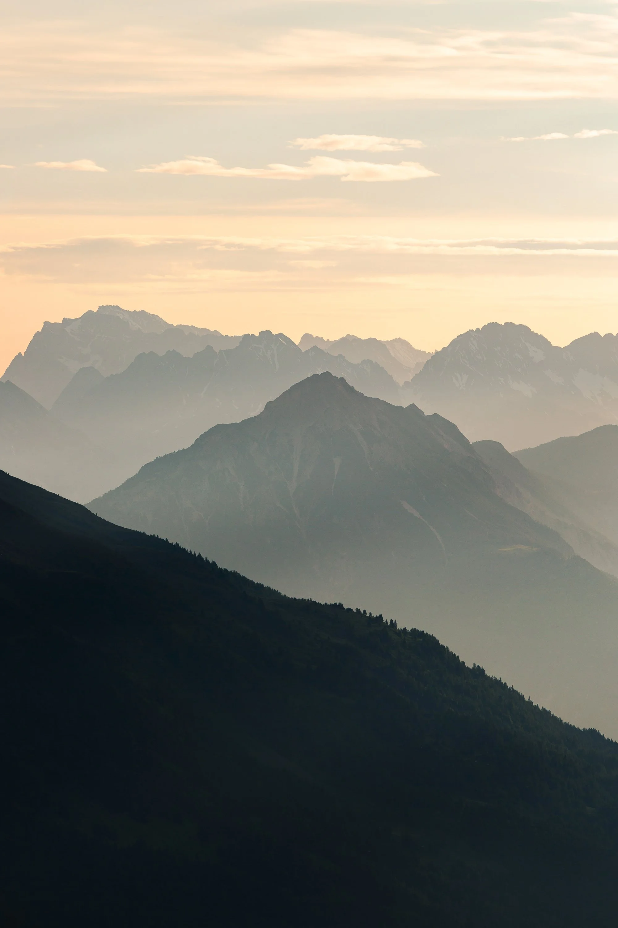 Mehrere Bergketten bei Sonnenaufgang oder Sonnenuntergang, mit bewölktem Himmel und Nebel im Tal