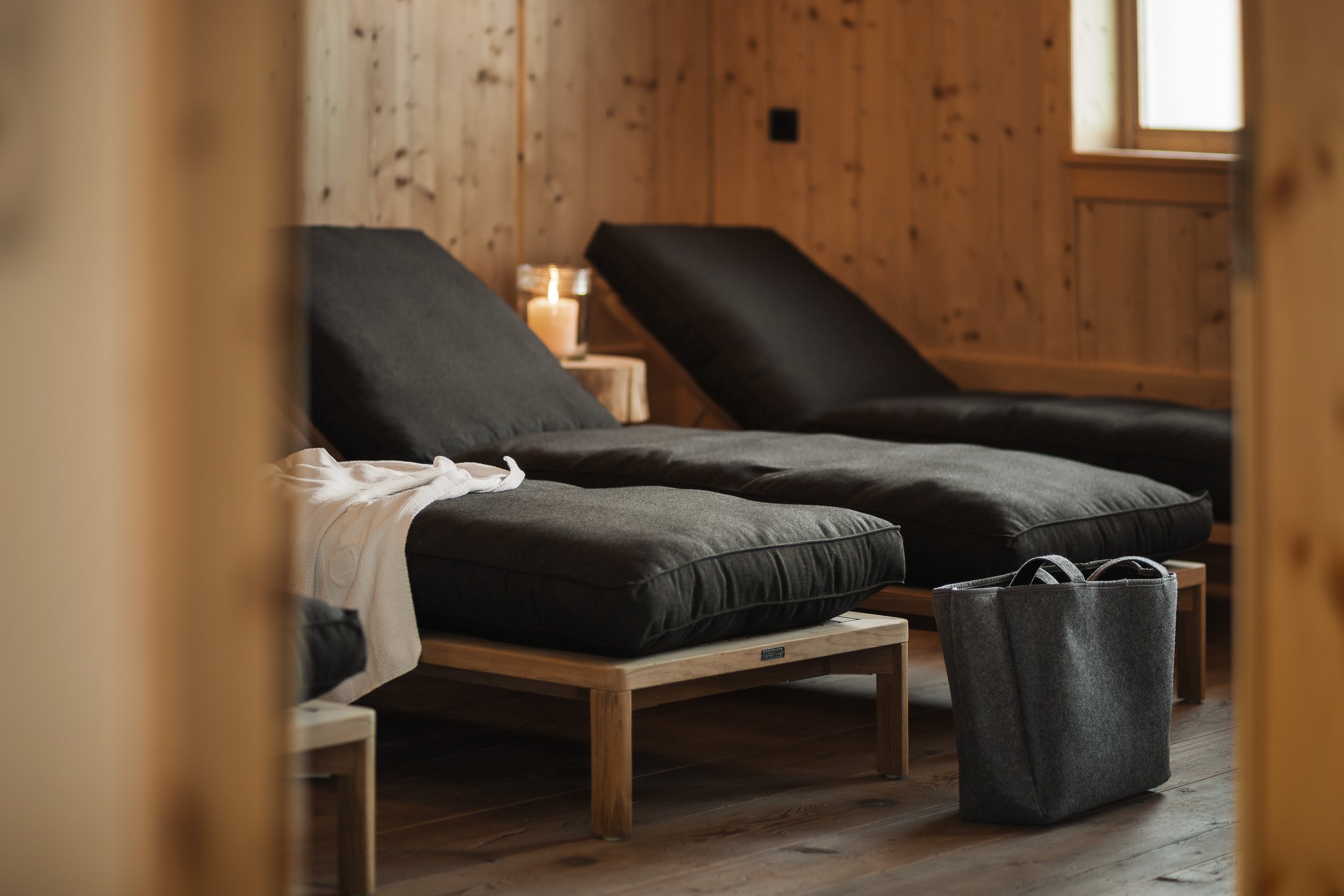 Sitzgelegenheiten mit schwarzen Kissen und einer Tasche in einem Holzraum, mit Kerze auf einem Tisch im Hintergrund.