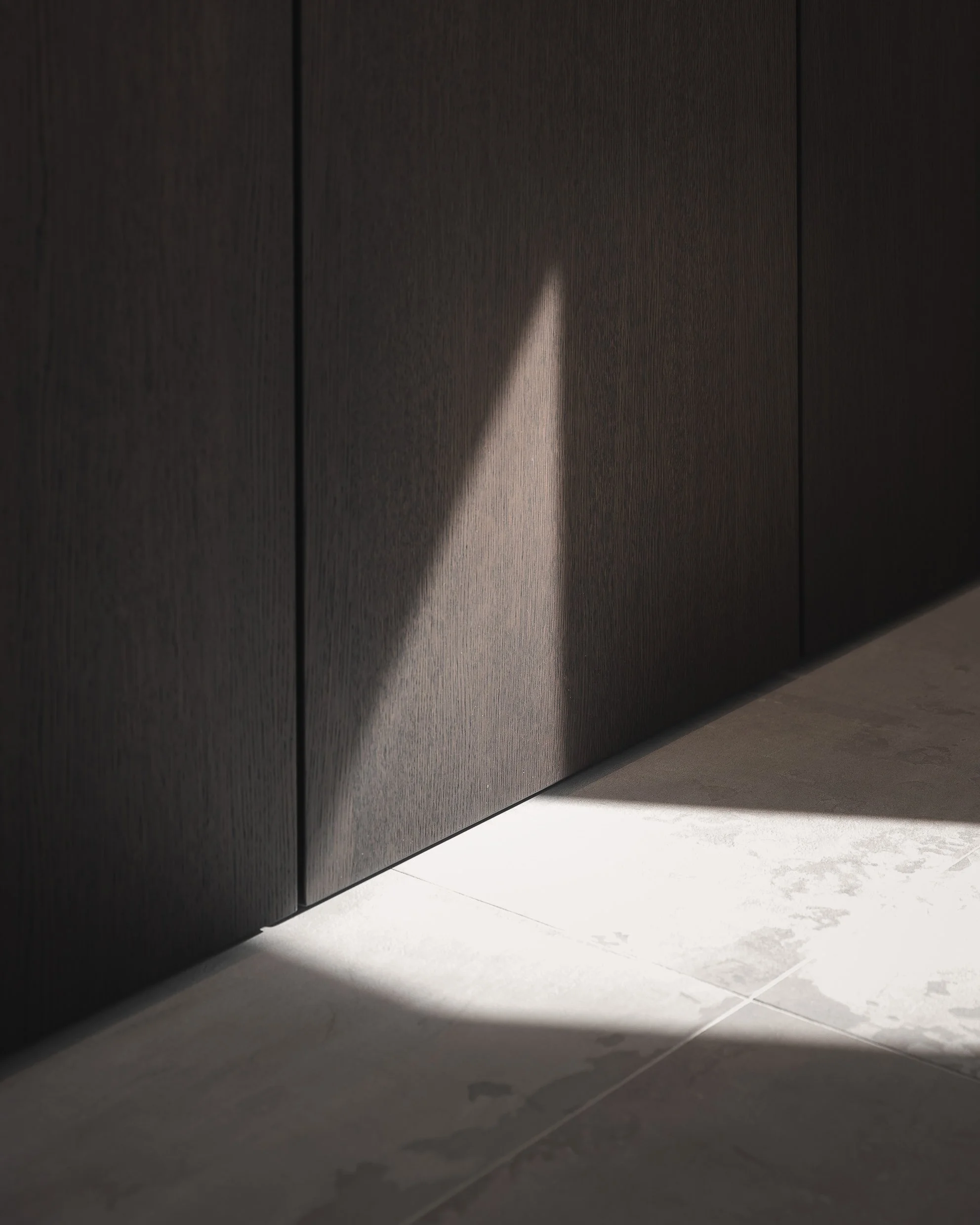 Nahaufnahme einer dunklen Holztür mit einem Schatten, der auf den Boden fällt.