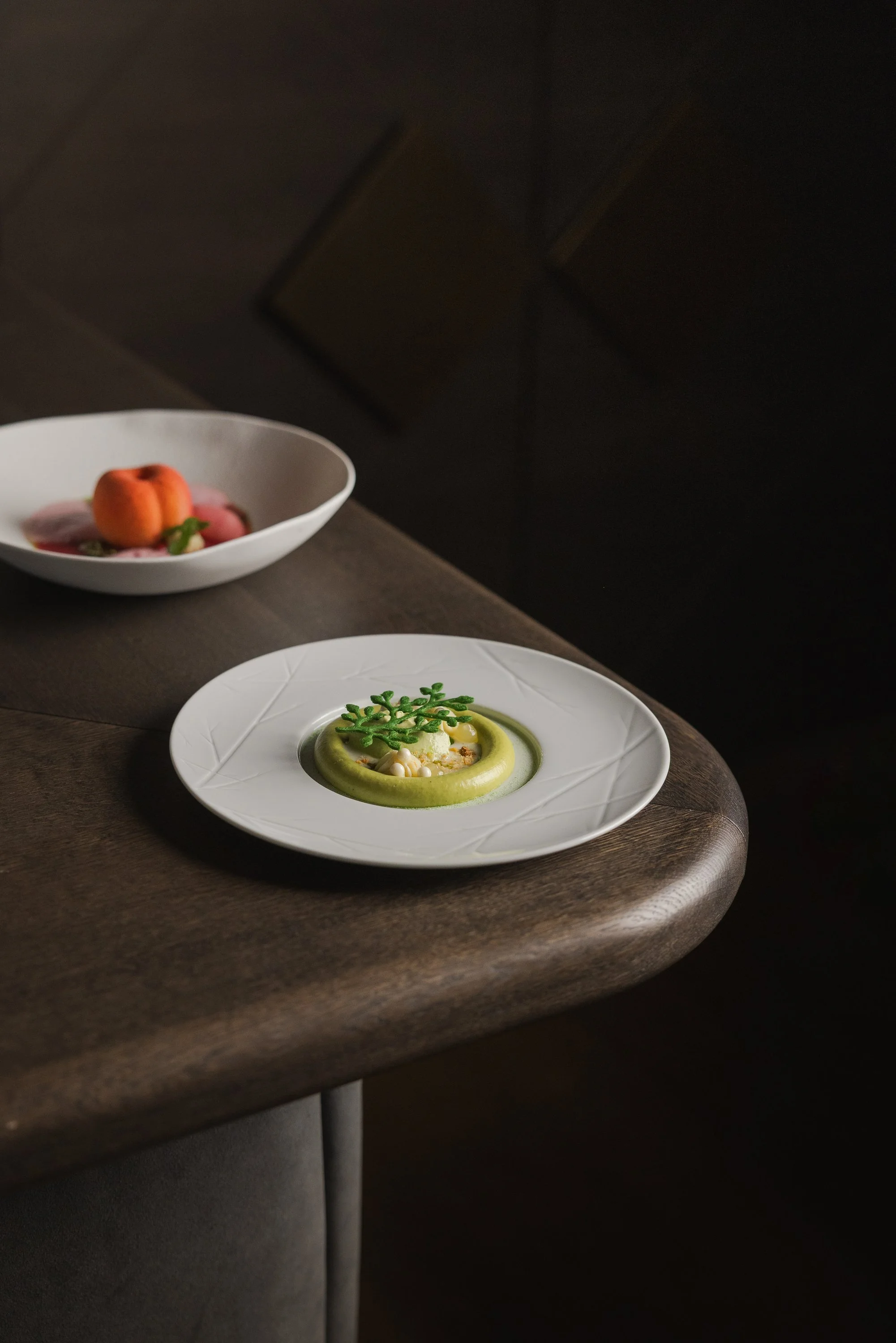 Feines Gericht mit grünem Püree und Dekoration, hintere Schale mit einem Dessert mit Pfirsich und Fruchtpüree.