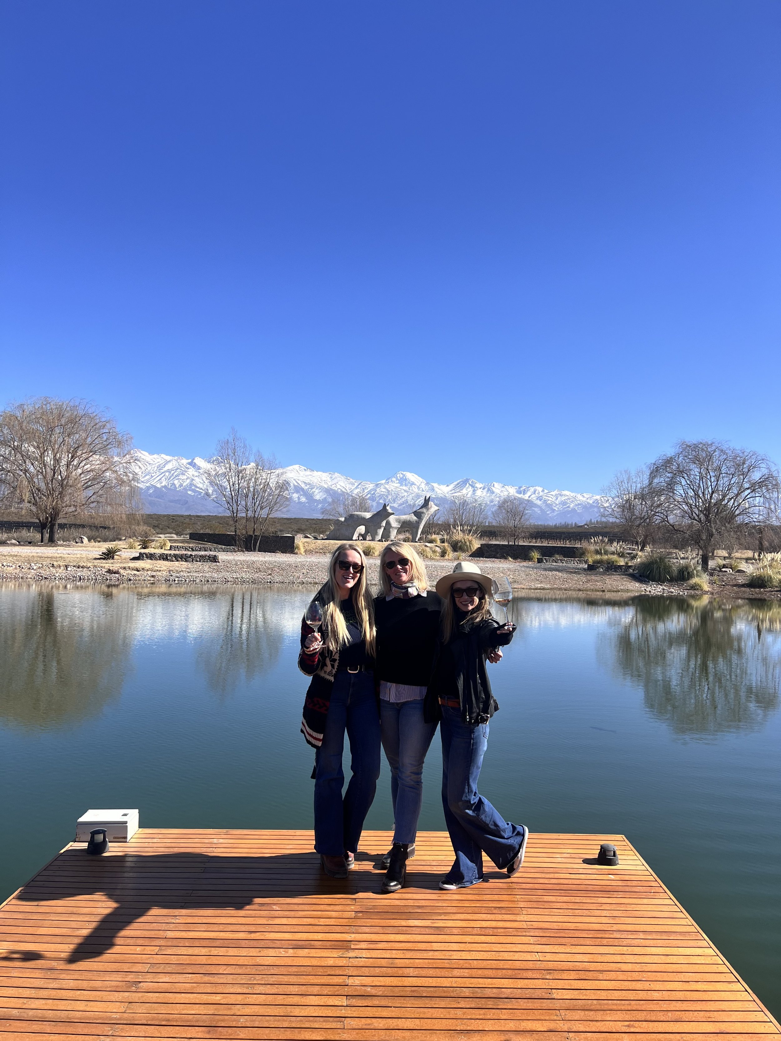 Three of our founders standing on a wooden deck by a lake in Argentina with mountains in the background under a clear blue sky.