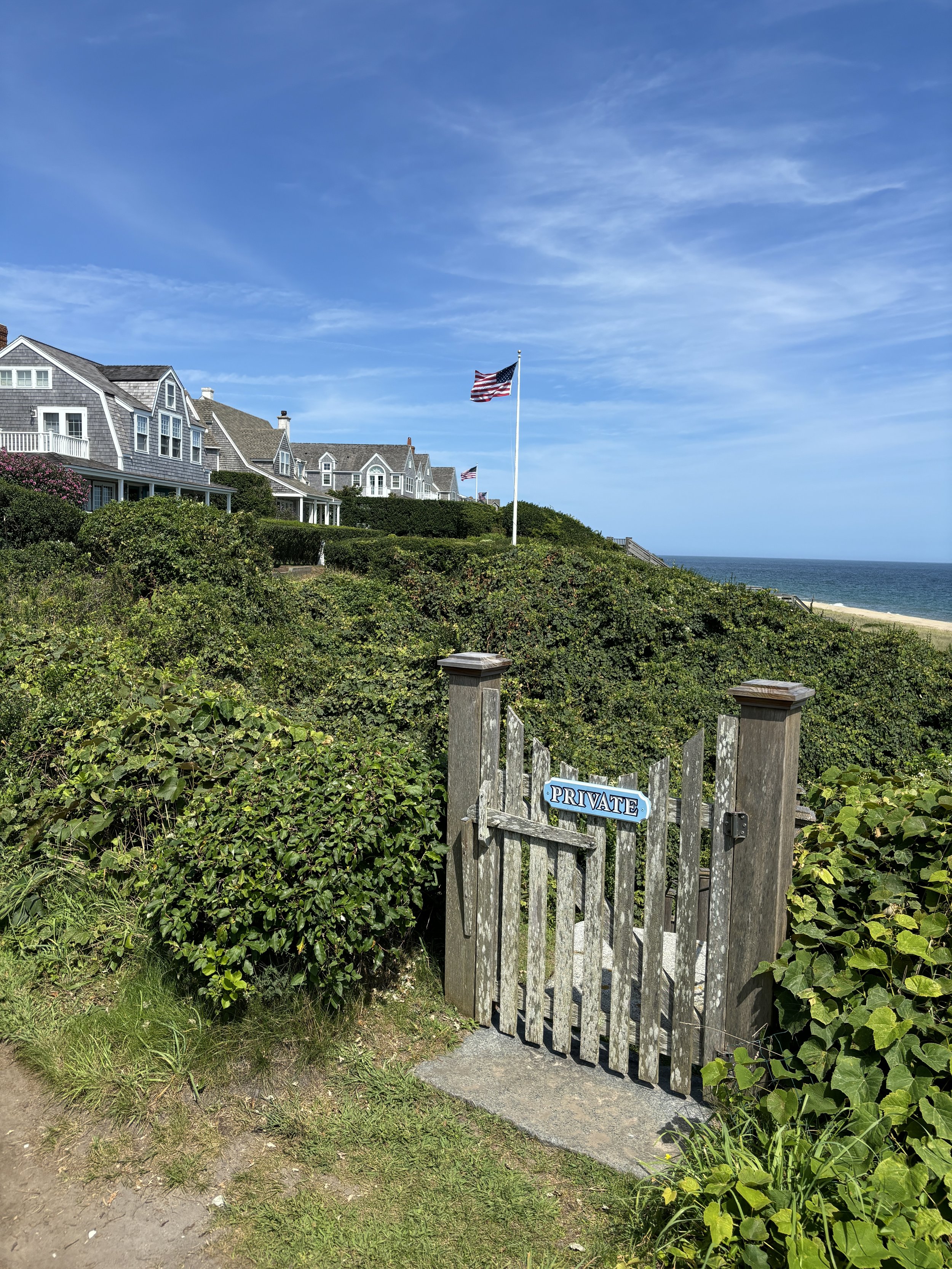 Beachside houses with American flags, a weathered wooden gate with a "Private" sign, ocean view.