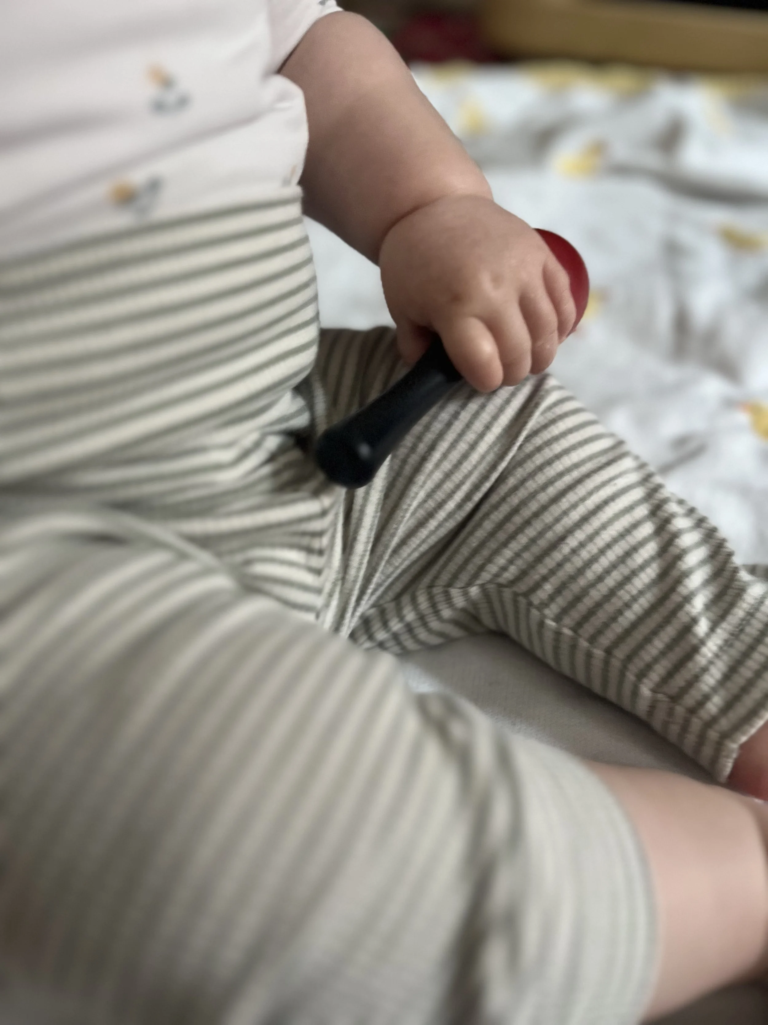 Nahaufnahme eines Babys, das eine kleine rote Wackelkugel hält, mit gestreifter Kleidung.