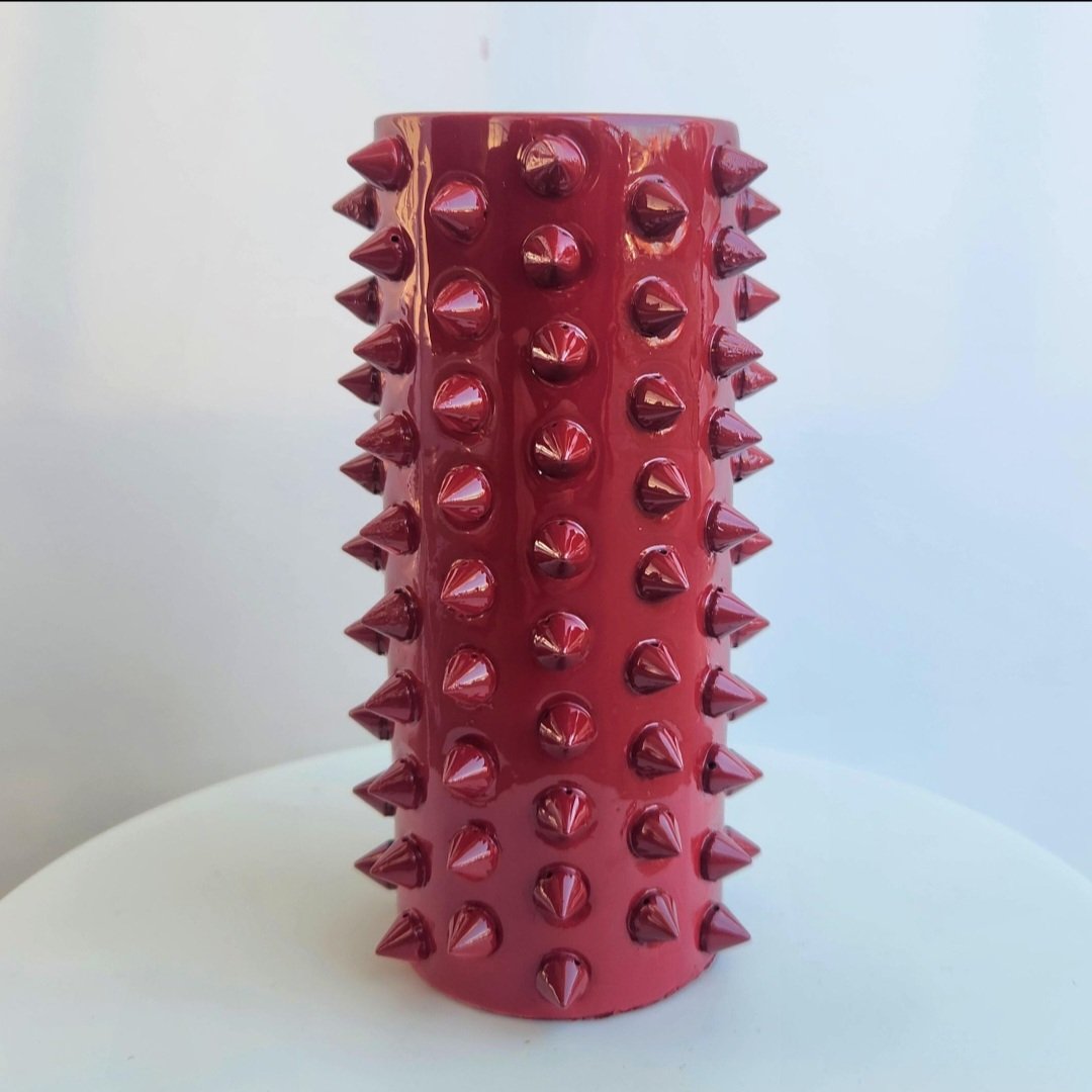 Red cylindrical vase with glossy finish, covered in evenly spaced conical spikes.
