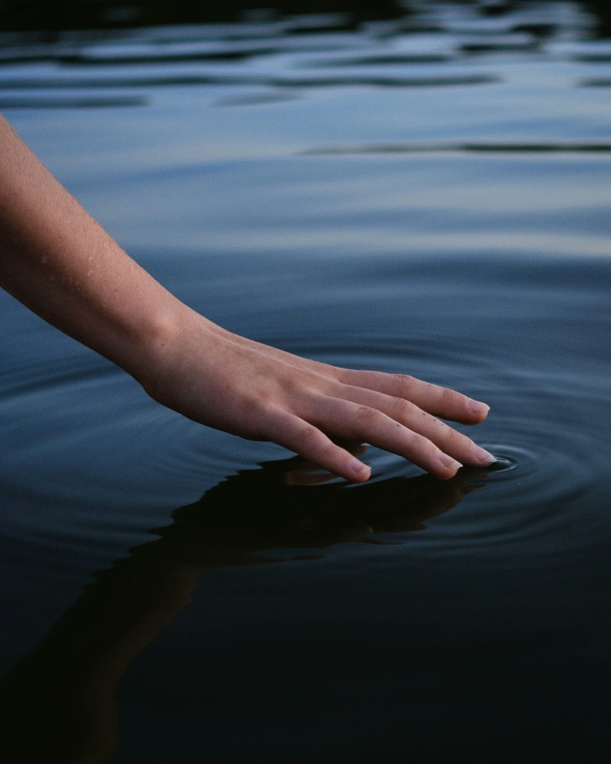 A hand gently touching the water's surface, creating ripples.