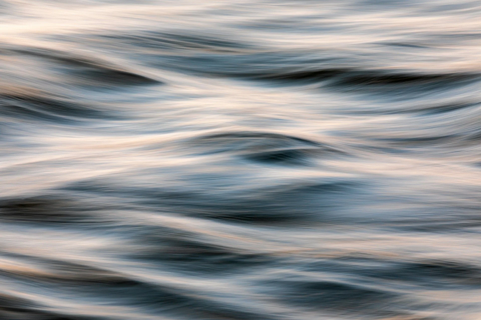 Abstract motion blur image of flowing water with blue and beige tones.