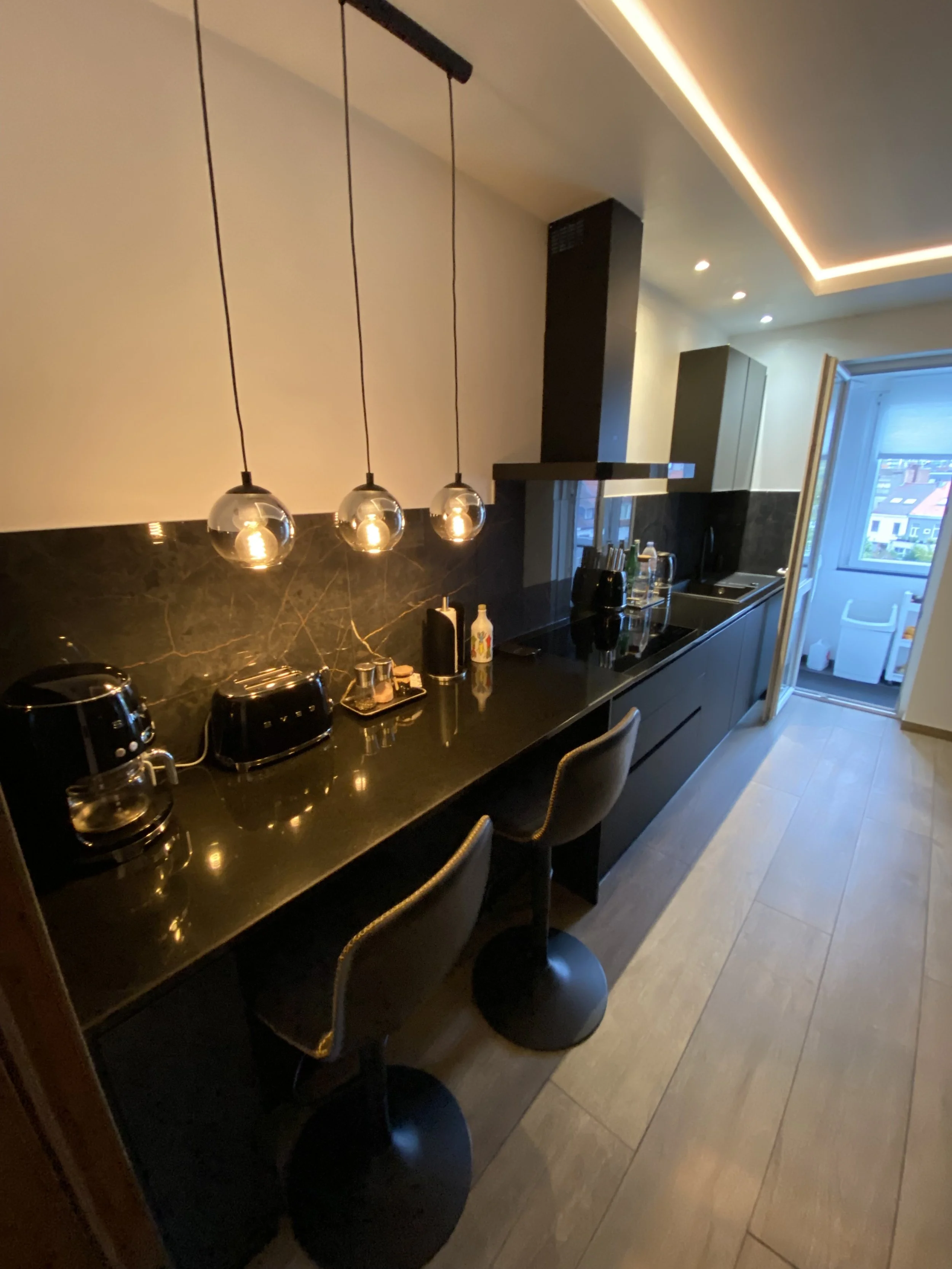 Cuisine noire design : Style chic avec plan de travail sombre, suspensions élégantes et touches dorées.